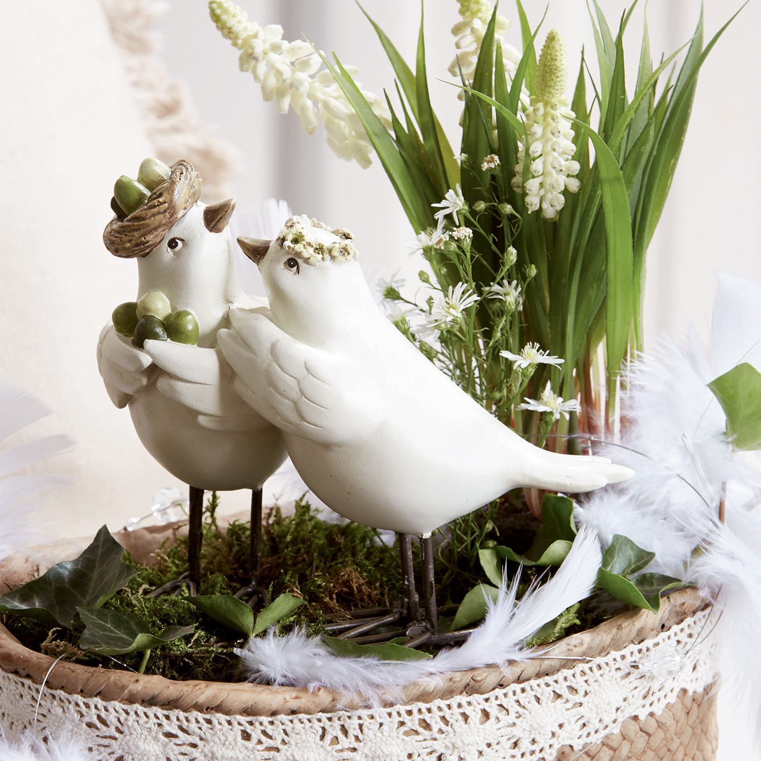 Couple d'oiseaux Orne Oiseaux décoratifs blancs en céramique sur pieds métalliques dans un panier en osier avec verdure et fleurs