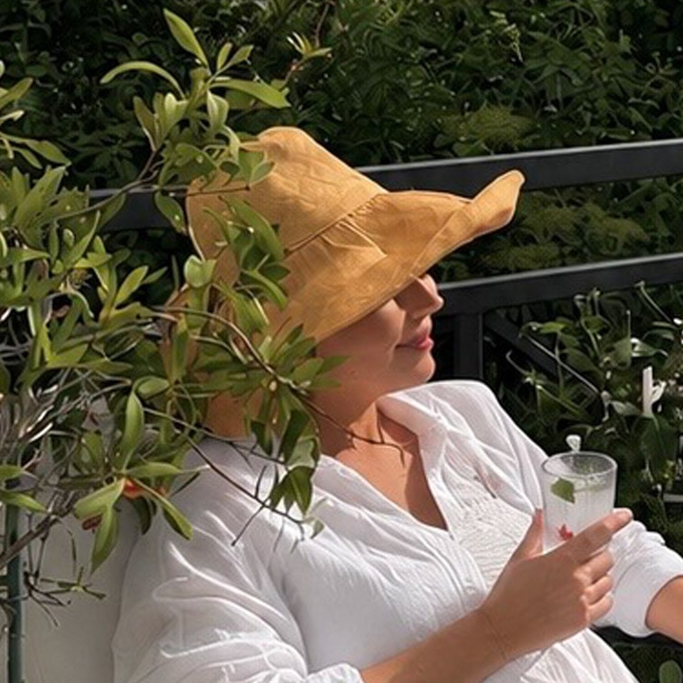 Femme en chemise blanche et chapeau de paille jaune se détend sur une terrasse avec une boisson