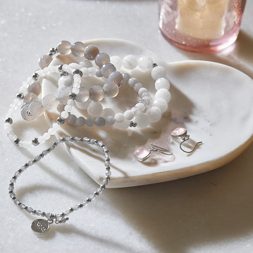 Ensemble de bijoux avec perles blanches et grises et boucles d'oreilles roses sur assiette en marbre