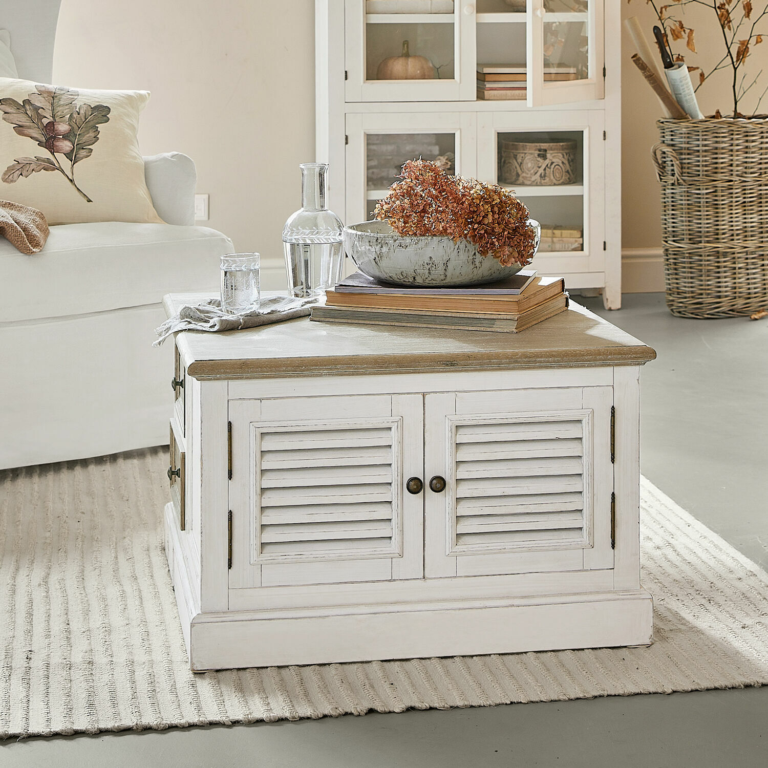 Table basse Cloverport Table basse en bois blanc avec tiroirs et décoration de fleurs séchées dans un salon lumineux
