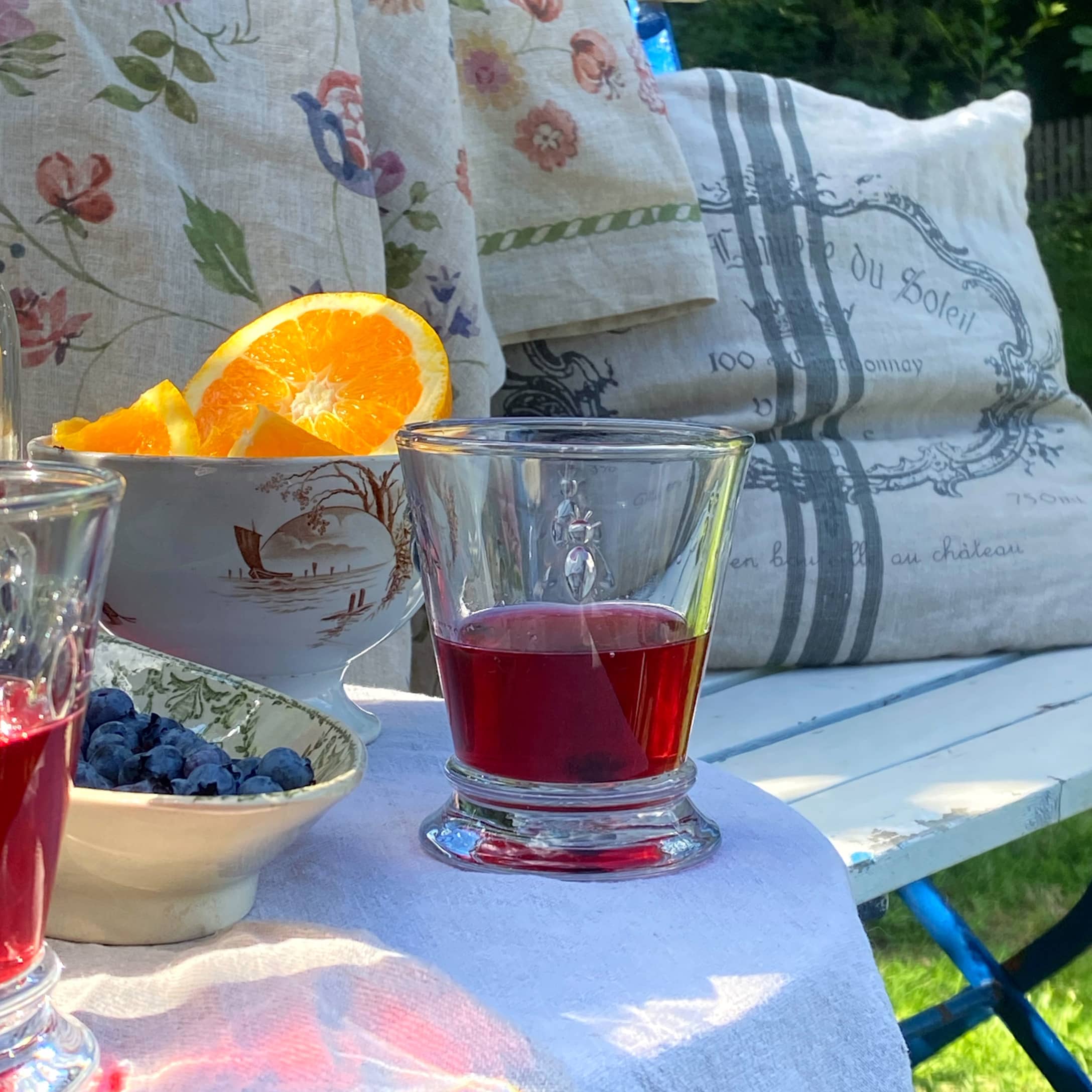 Verre avec boisson rouge sur nappe blanche, fruits et coussin décoratif en arrière-plan