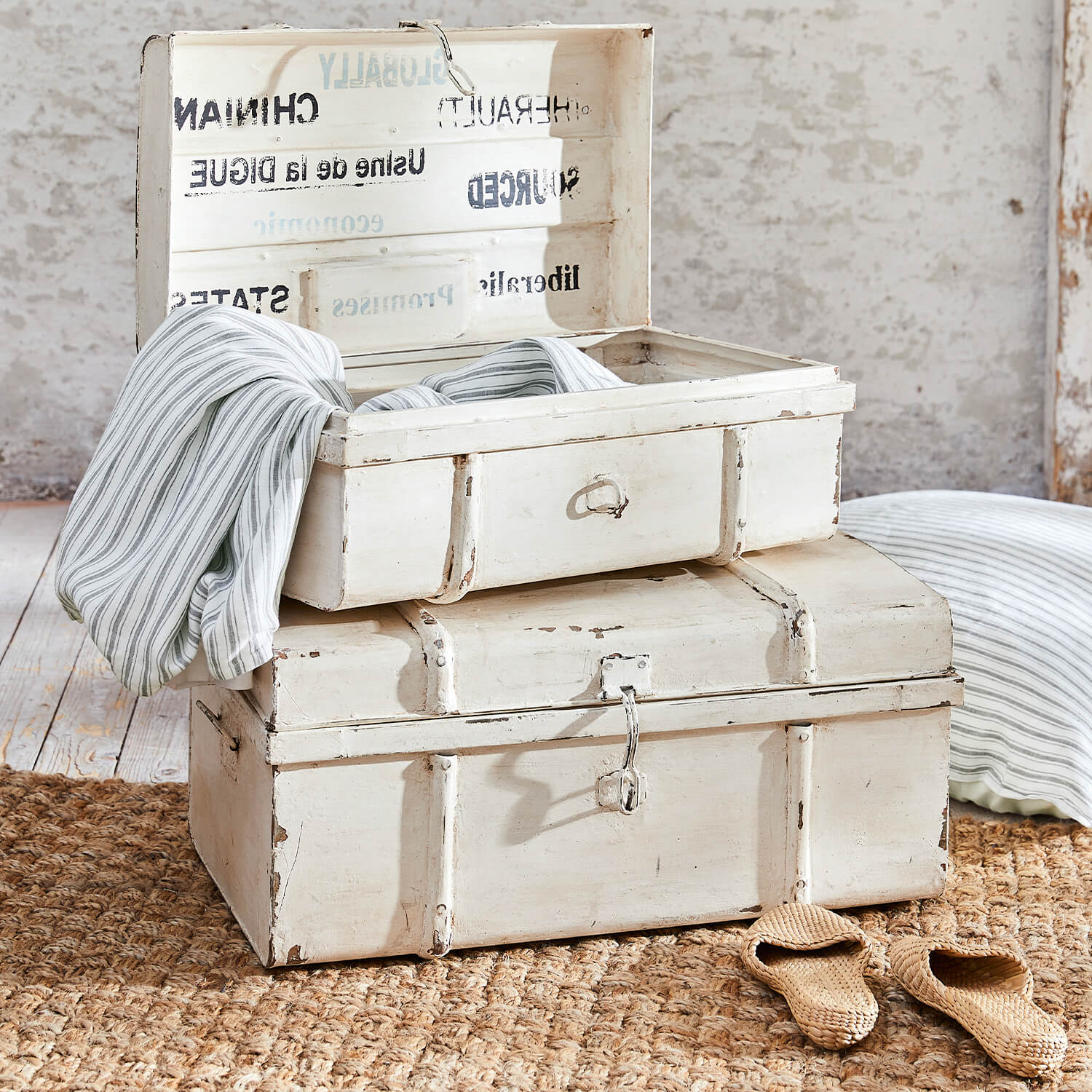 Coffres en bois blanc vieilli posés sur un tapis en jute avec tissu rayé à l'intérieur