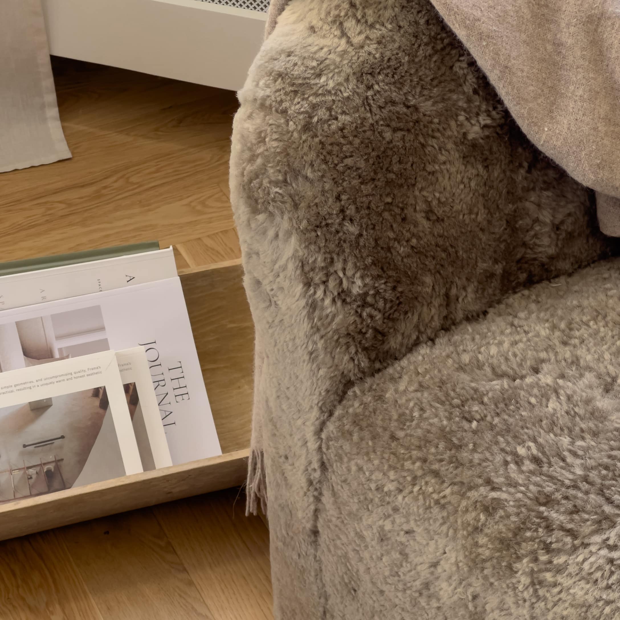 Plaid gris doux en fausse fourrure sur fauteuil près d'un plateau en bois avec magazines déco