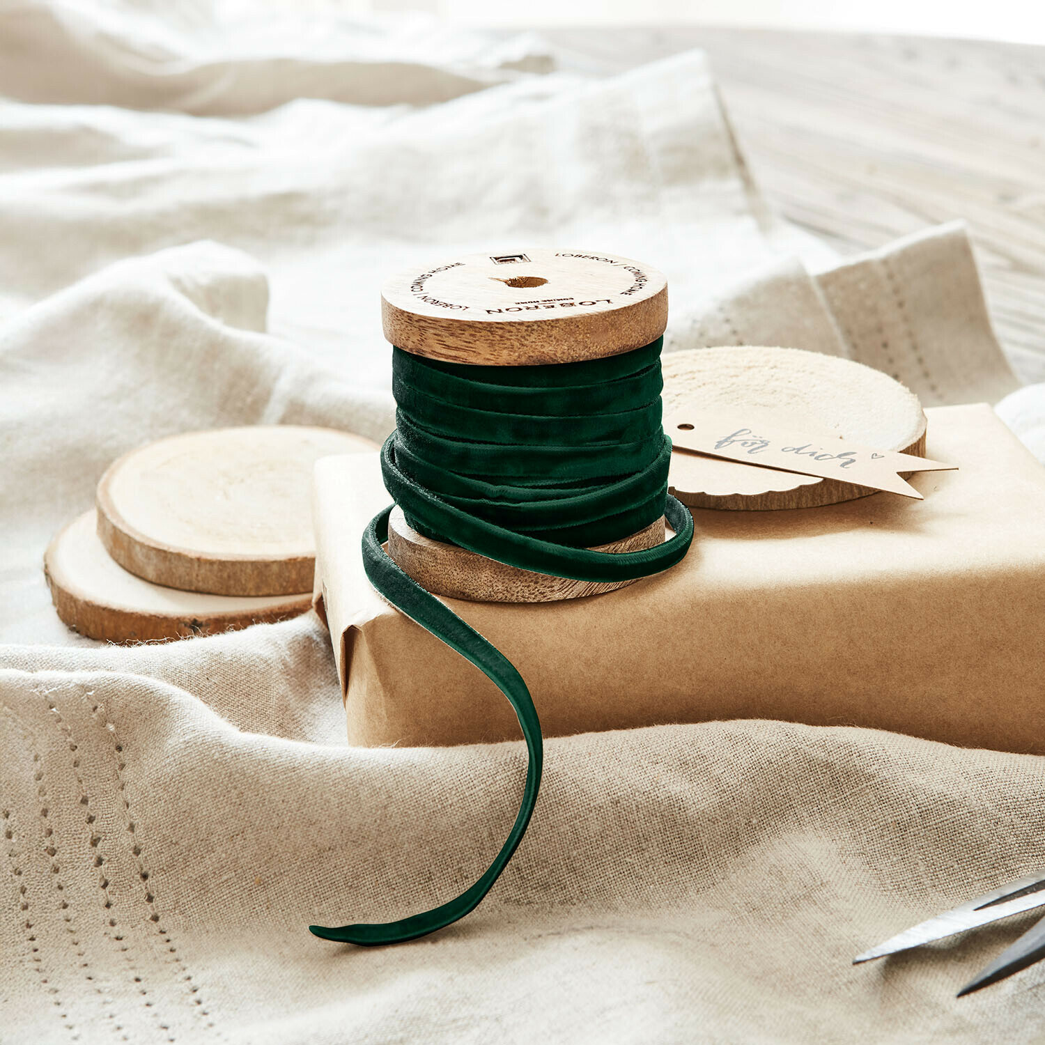 Ruban de velours Olessa Ruban en velours vert enroulé sur une bobine en bois posé sur un papier kraft et tissu naturel pour emballage cadeau