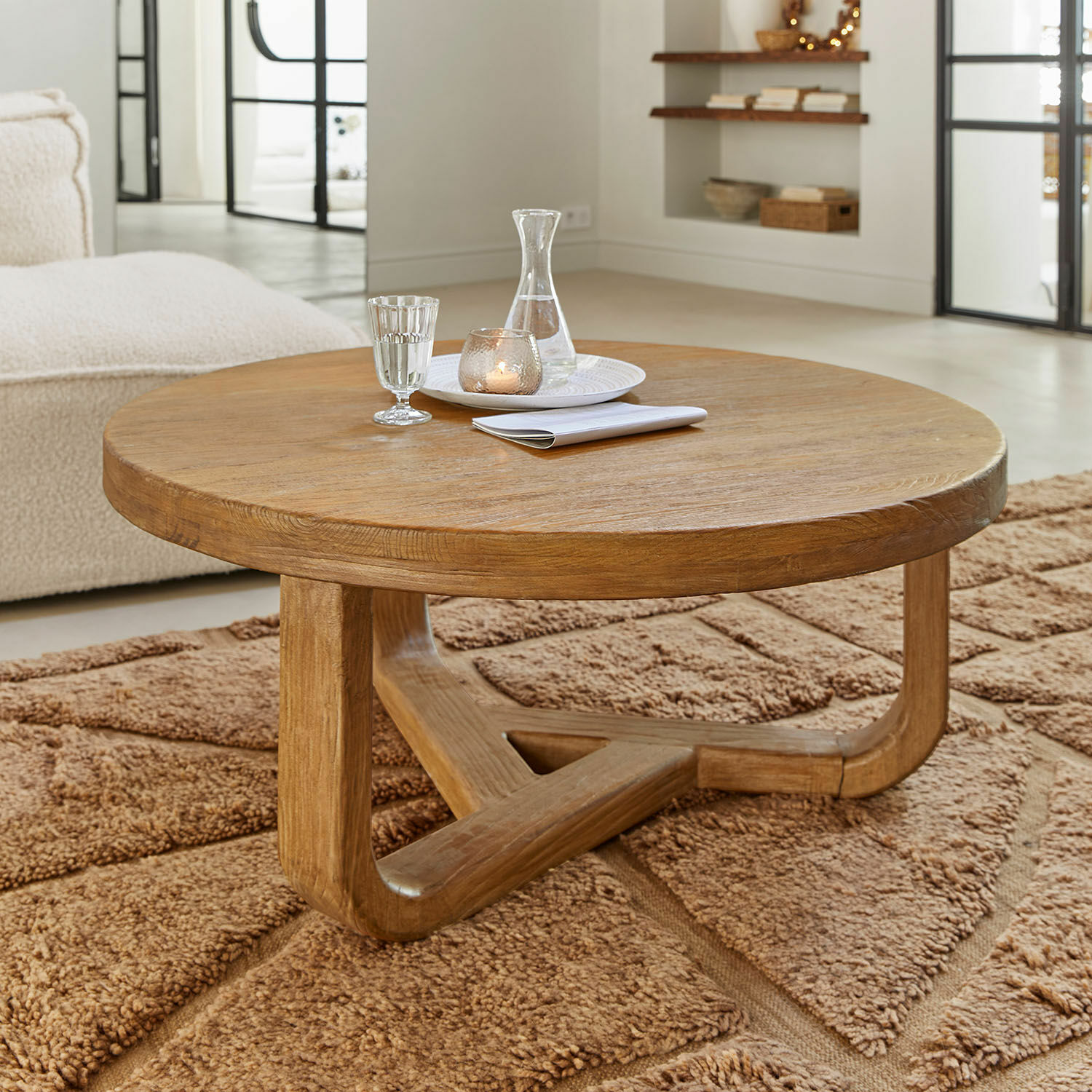 Table basse Trésorique Table basse ronde en chêne naturel posée sur un tapis marron moelleux dans un salon lumineux