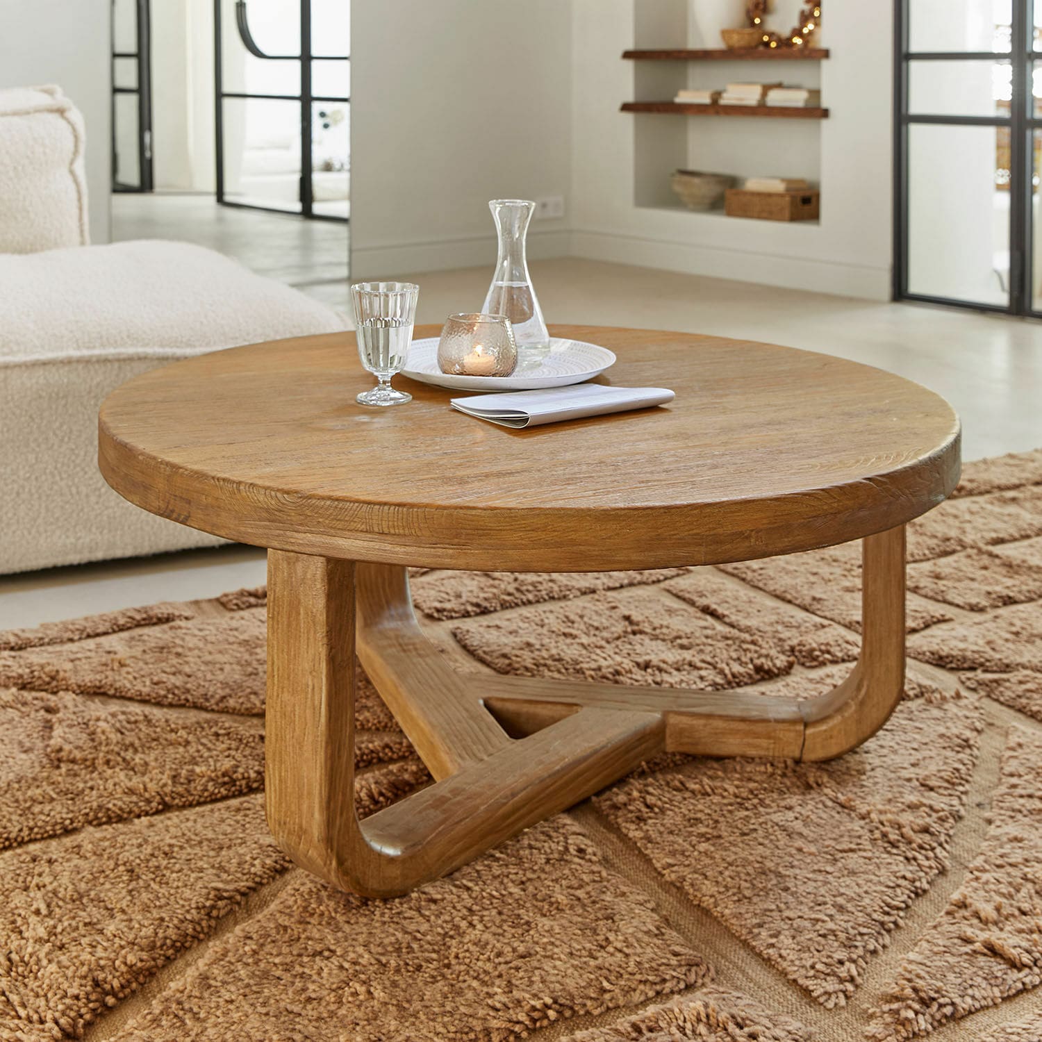 Table basse Trésorique Table basse ronde en chêne naturel posée sur un tapis marron moelleux dans un salon lumineux