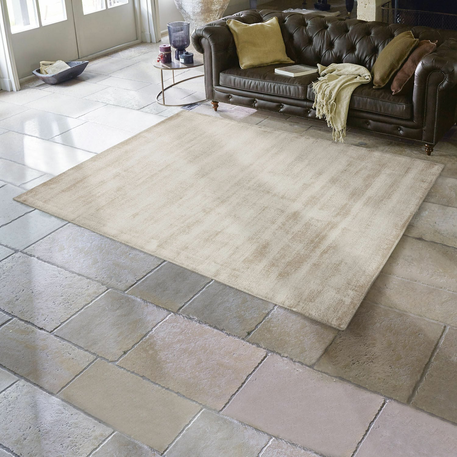 Tapis Mariselle Tapis beige en tissu doux sur sol en pierre dans un salon avec canapé en cuir marron foncé