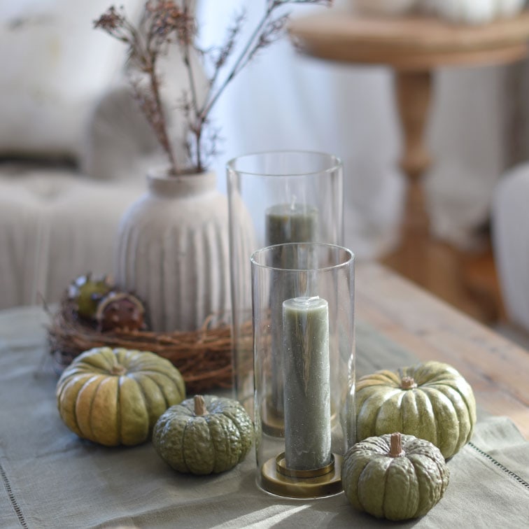 Bougies vertes décoratives et citrouilles sur des photophores en verre sur une table en bois au style naturel