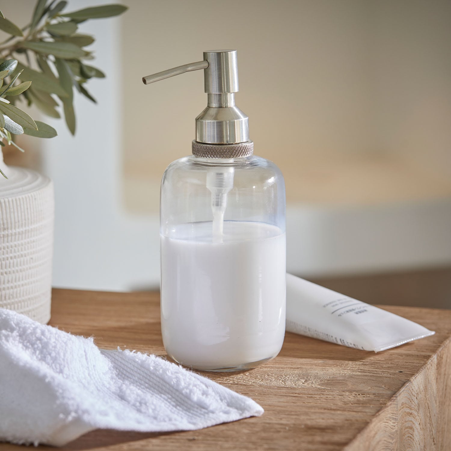 Distributeur de savon transparent en acier inoxydable avec liquide blanc sur surface en bois