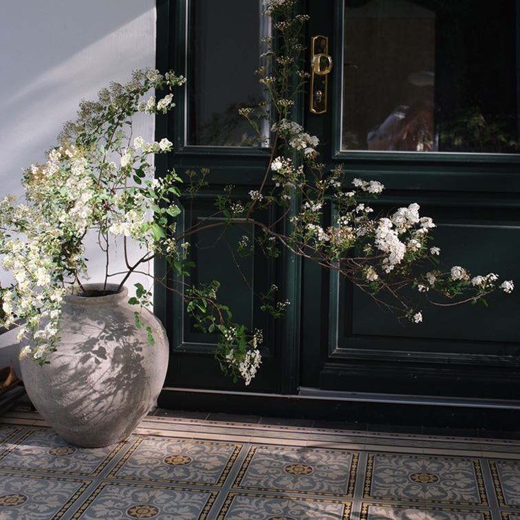 Grand vase en céramique avec fleurs blanches devant une porte sombre et un sol carrelé décoratif