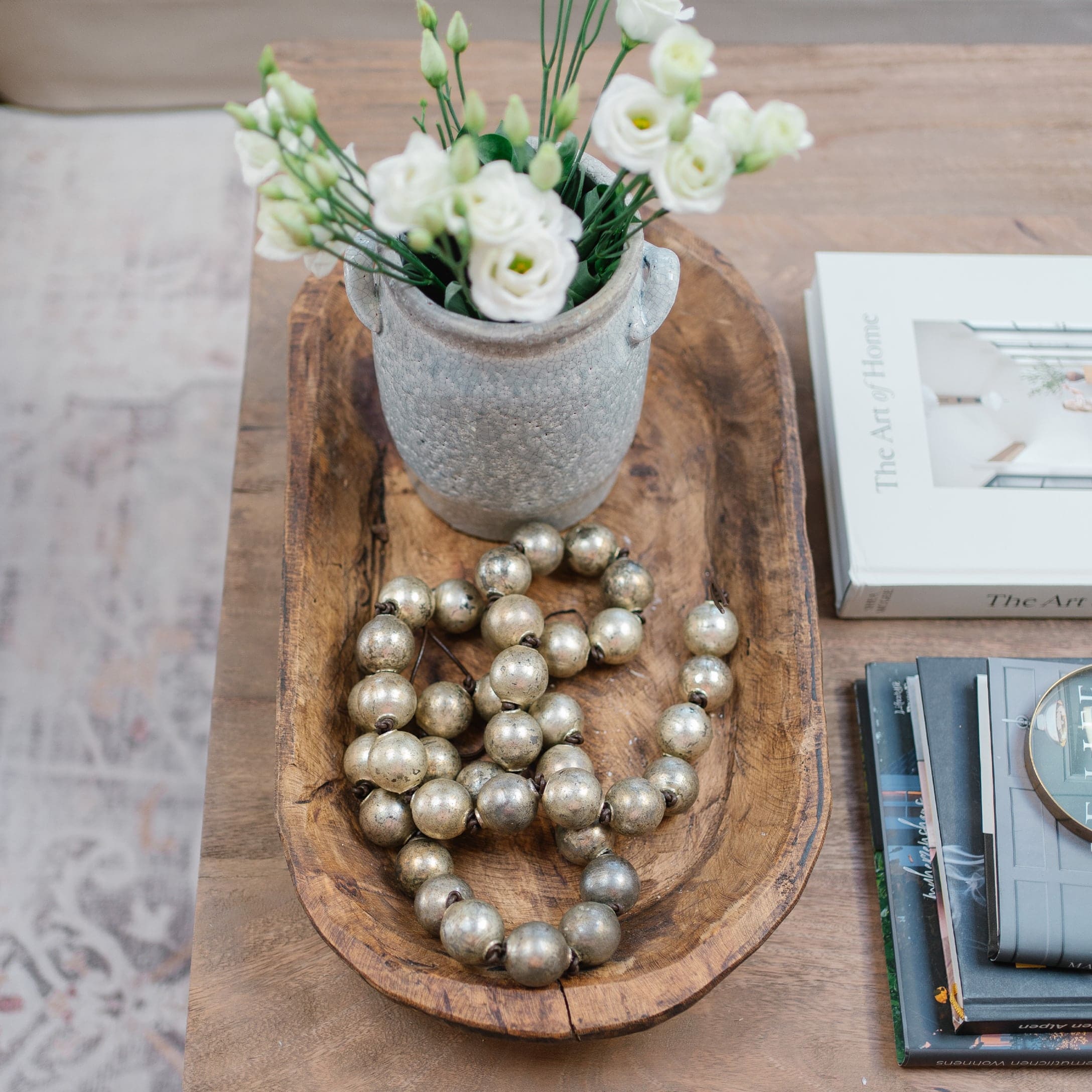 Plat en bois avec un vase en céramique grise, fleurs blanches et collier décoratif en perles métalliques