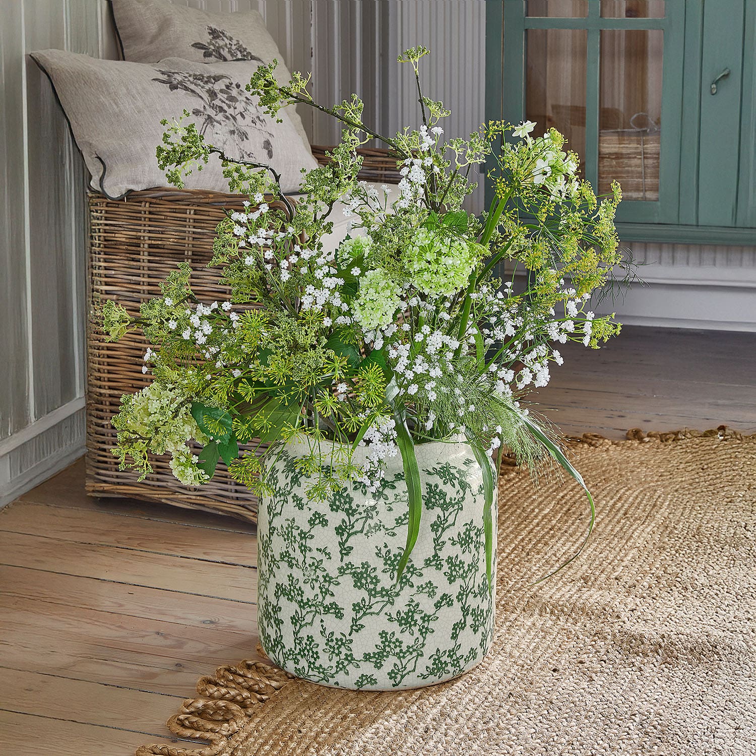 Vase en céramique à motif vert avec fleurs blanches et vertes sur un sol en bois clair