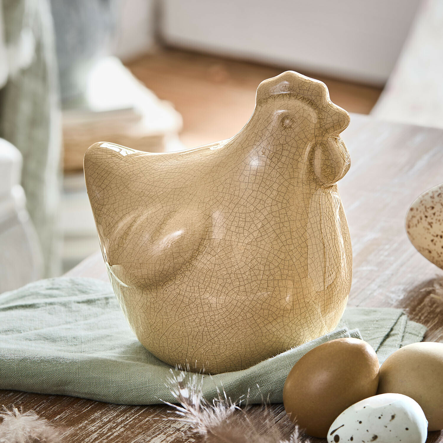 Figurine décorative Poule Roisenn Figurine de poule en céramique beige craquelée posée sur un tissu vert avec des œufs décoratifs