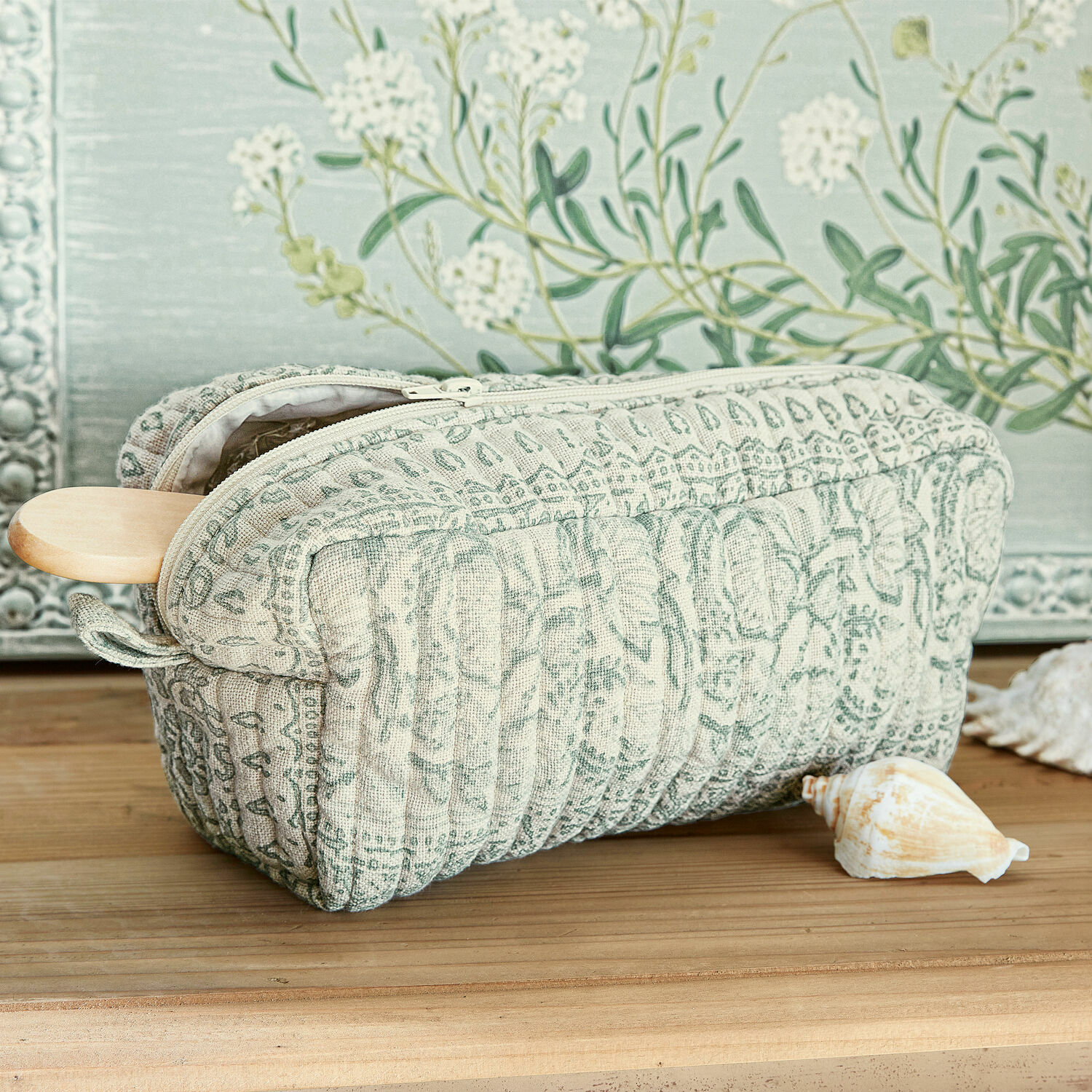 Pochette Saône Trousse matelassée en tissu beige et vert avec motif, posée sur une table en bois avec coquillage