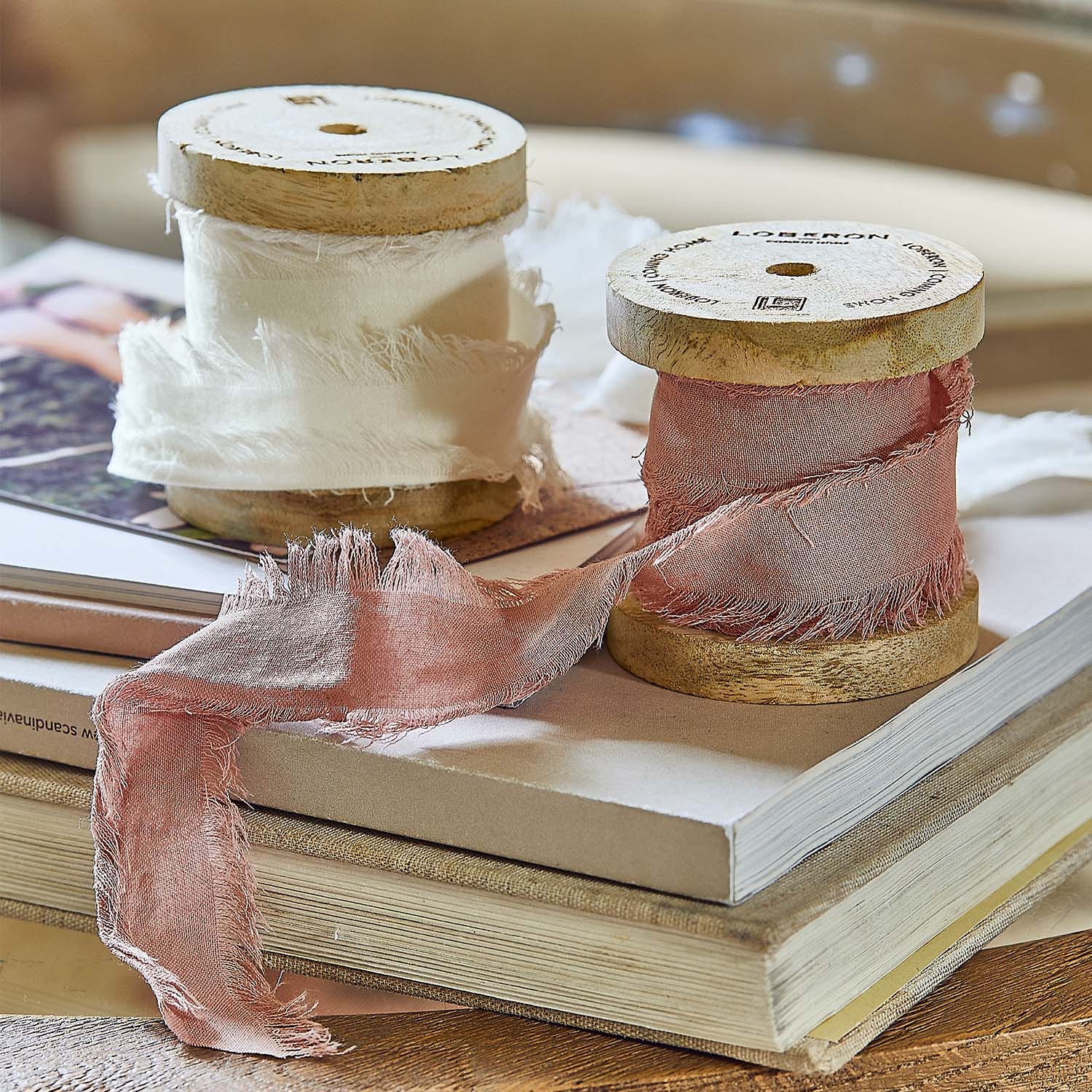 Bobines en bois avec tissu fin blanc et rose posées sur une pile de livres pour décoration intérieure