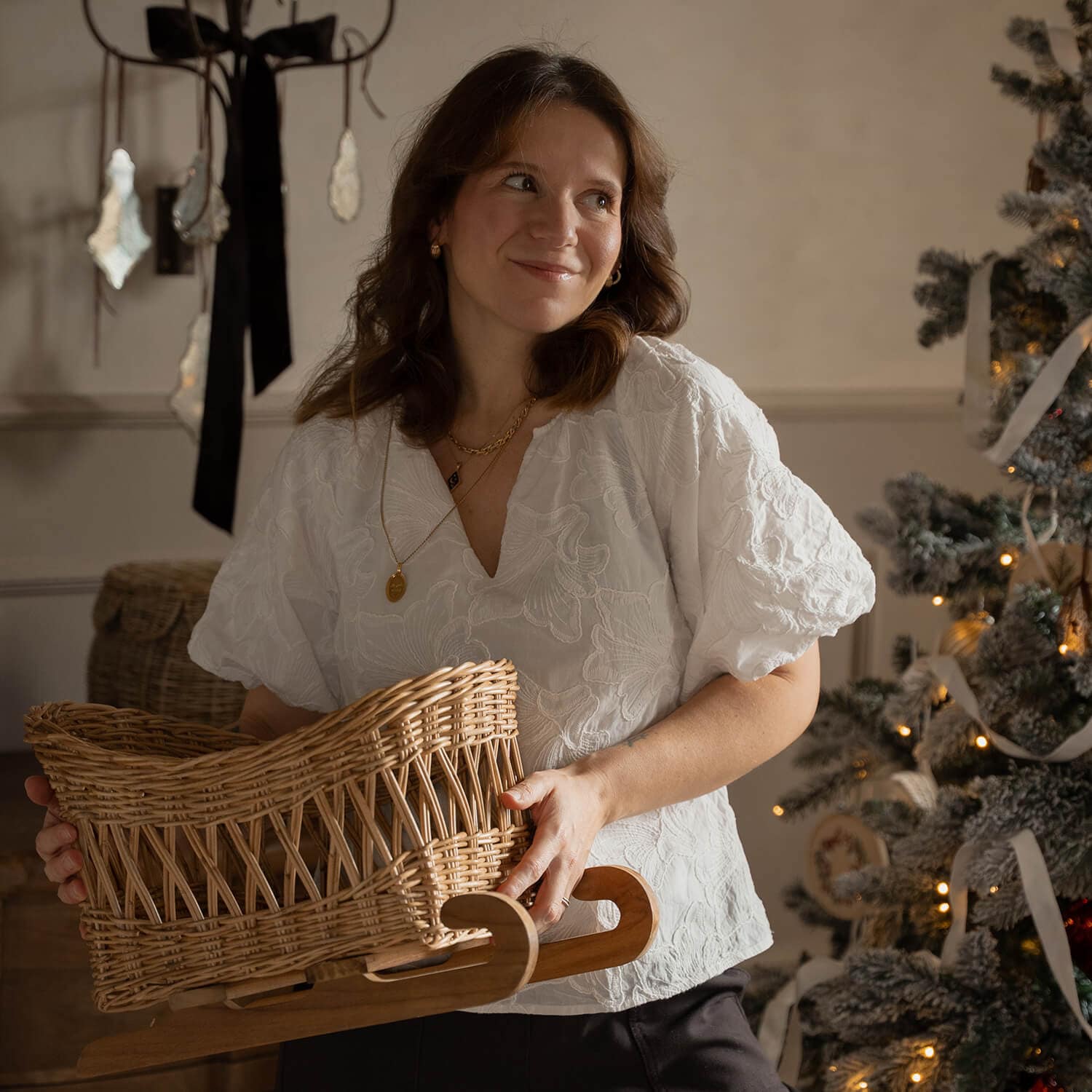 Femme en blouse blanche tenant un traîneau en osier avec base en bois près d'un sapin décoré