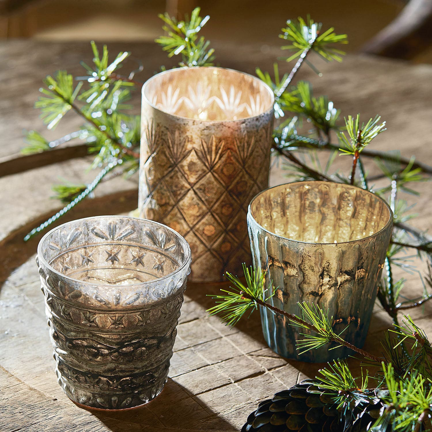 Lot de 3 photophores Ginai Ensemble de trois photophores en verre avec motifs décoratifs en tons bruns et gris sur une table en bois