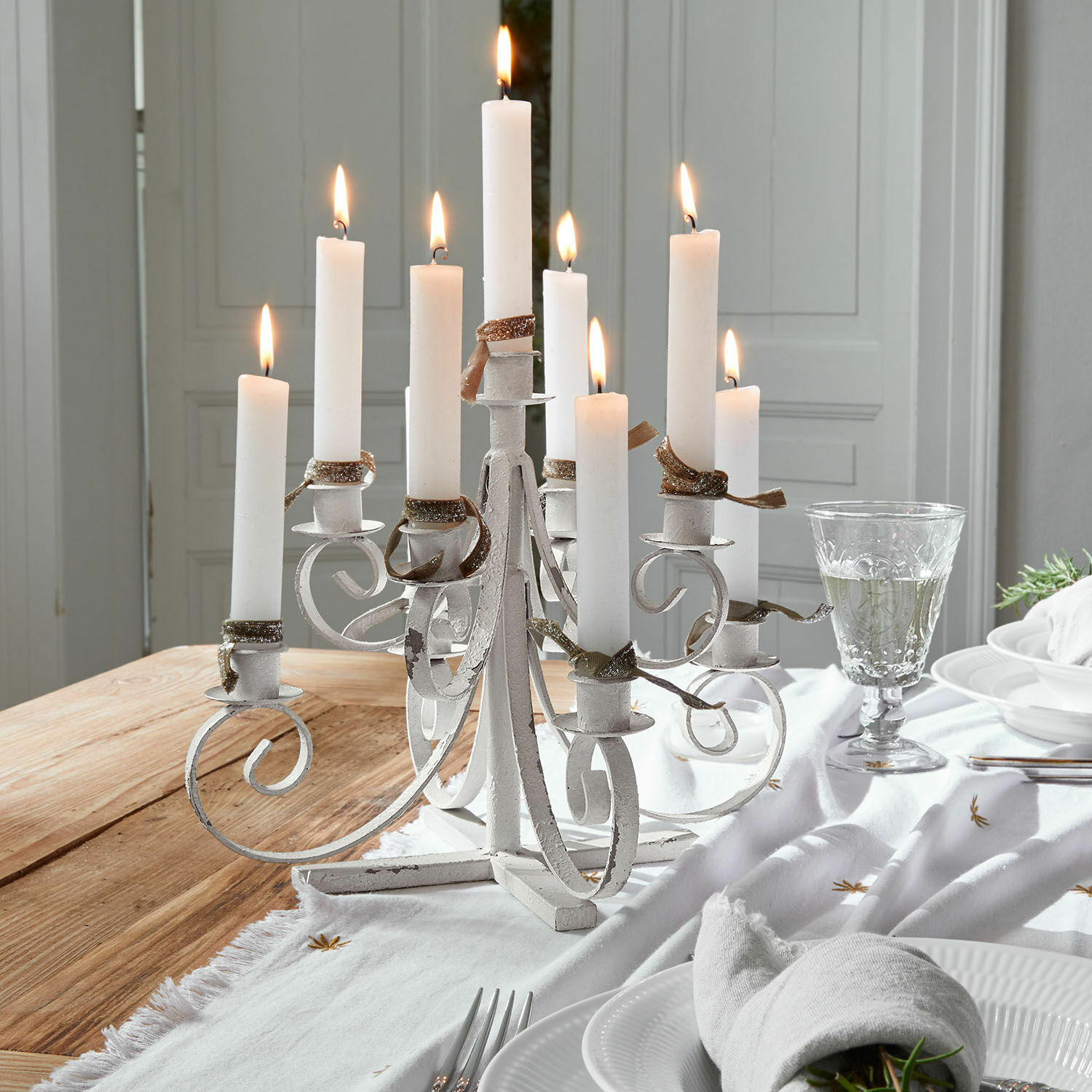Bougeoir Siolagh Chandelier blanc en métal avec neuf bougies allumées sur une table en bois décorée pour repas