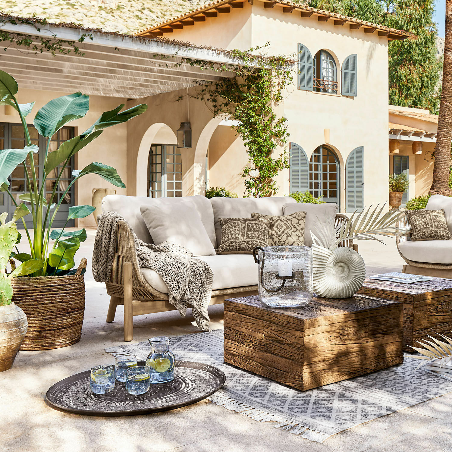 Canapé FSC®-100% Belvidere Ensemble de mobilier d'extérieur avec canapé beige, table en bois et décorations sur terrasse ensoleillée