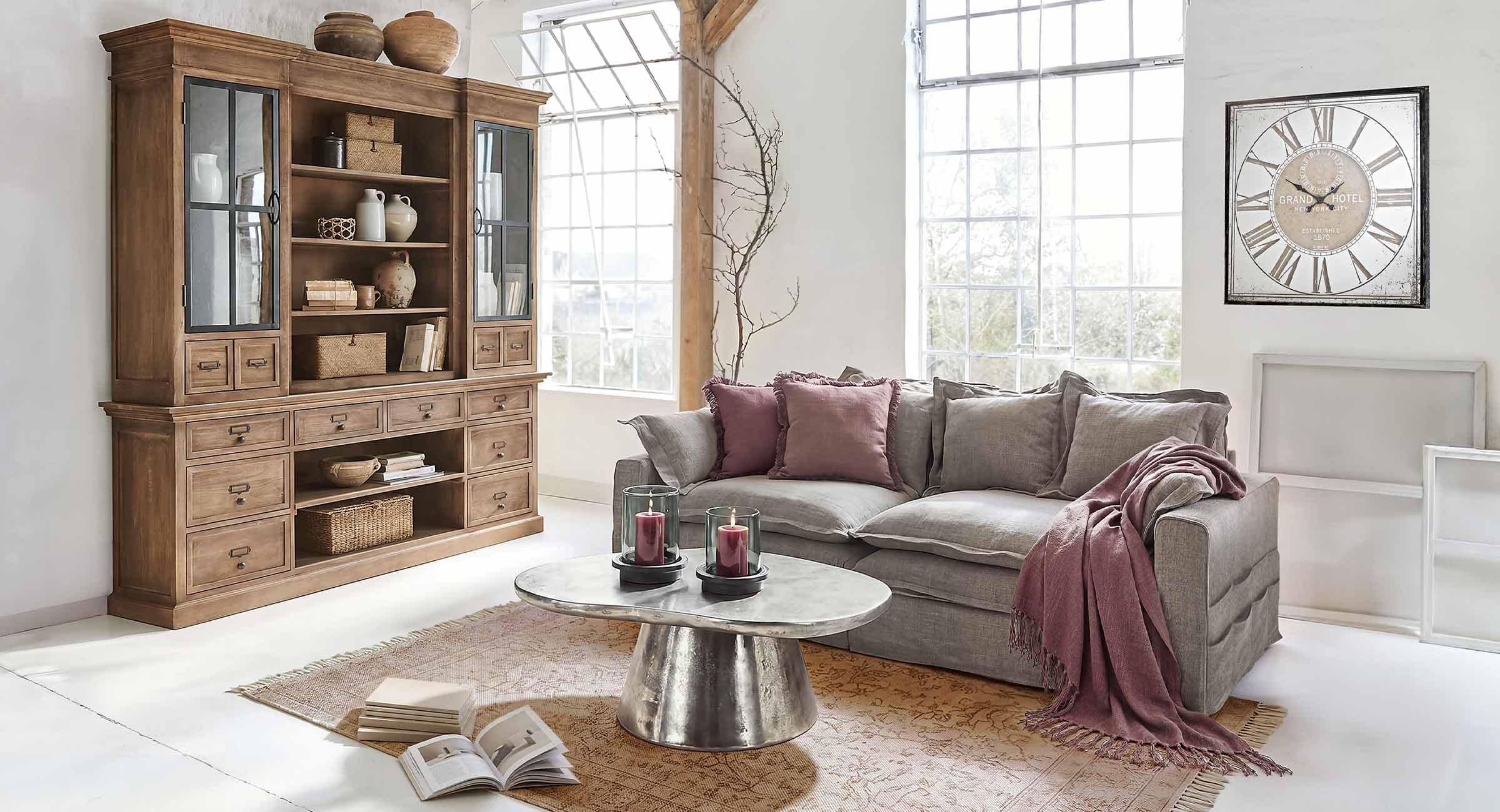 Salon lumineux avec canapé gris, coussins bordeaux et meuble en bois vintage avec décorations