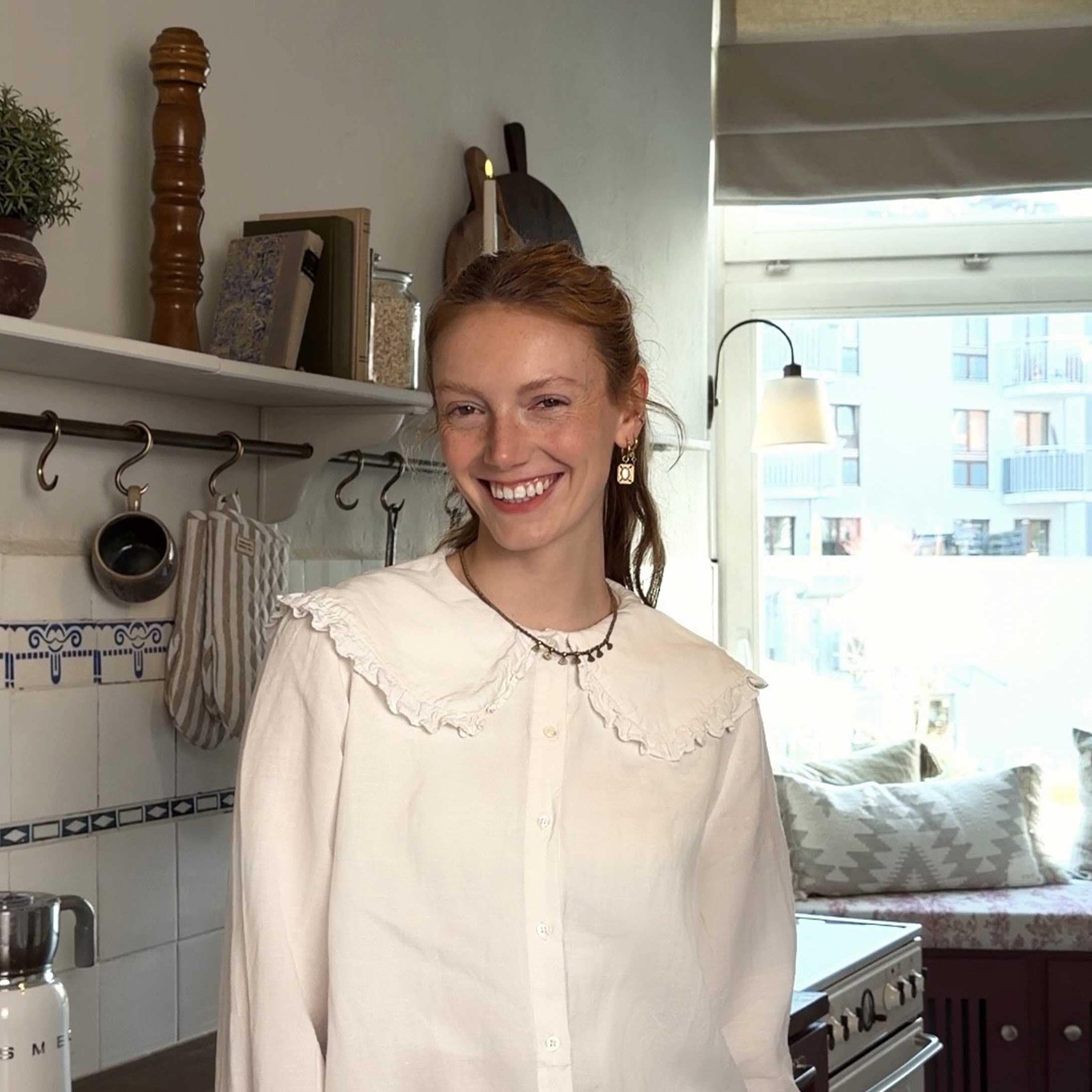 Femme souriante en chemisier blanc à volants dans une cuisine lumineuse avec accessoires décoratifs