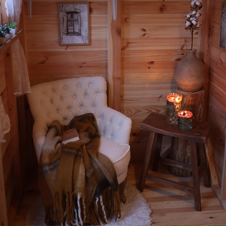 Coin cosy avec fauteuil blanc capitonné, plaid marron et tabouret en bois avec bougies allumées