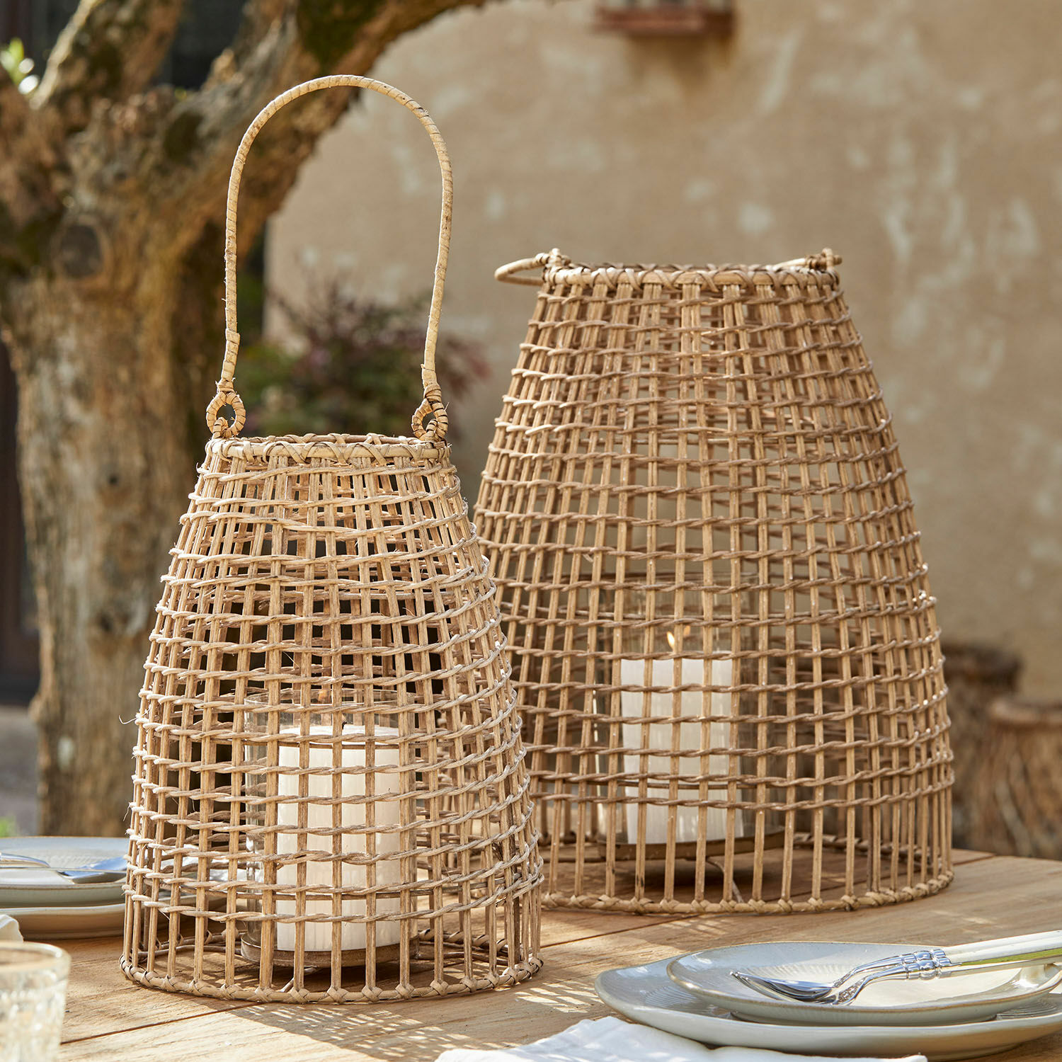 Lot de 2 lanternes Hillendale Deux lanternes en rotin naturel avec bougies blanches sur une table en bois en extérieur
