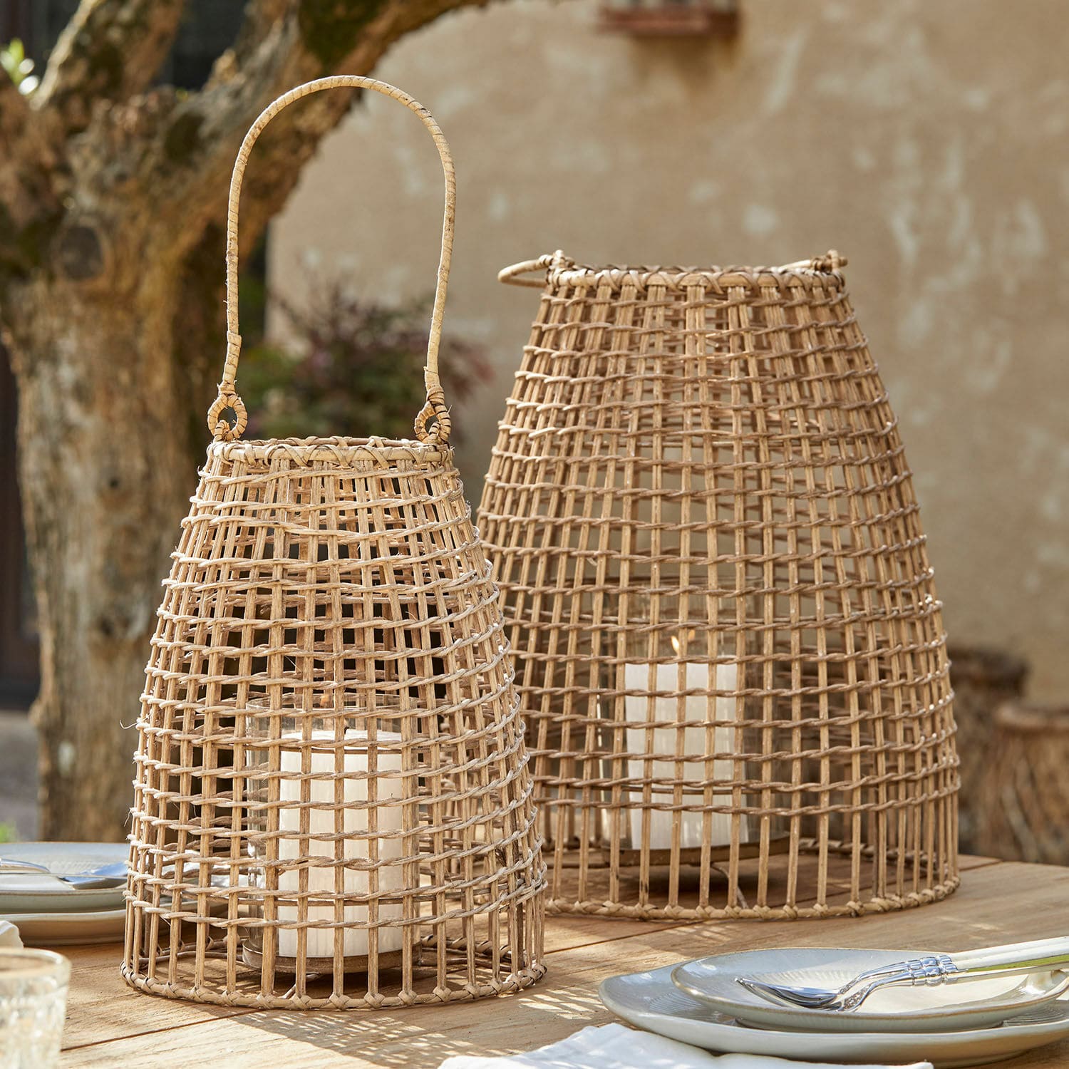 Lot de 2 lanternes Hillendale Deux lanternes en rotin naturel avec bougies blanches sur une table en bois en extérieur