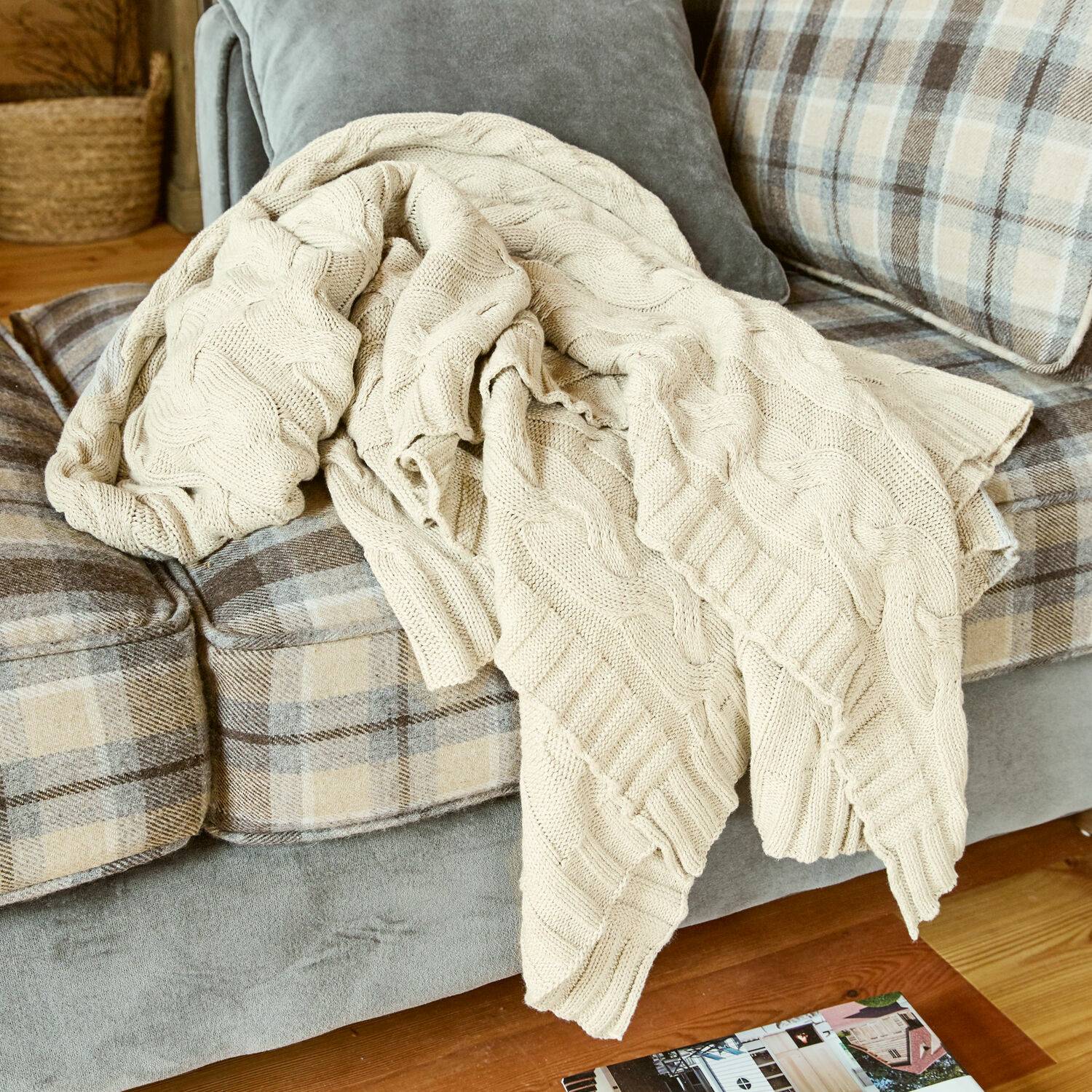Plaid Arnhem Plaid beige en coton tricoté posé sur un canapé gris à carreaux beige dans un salon