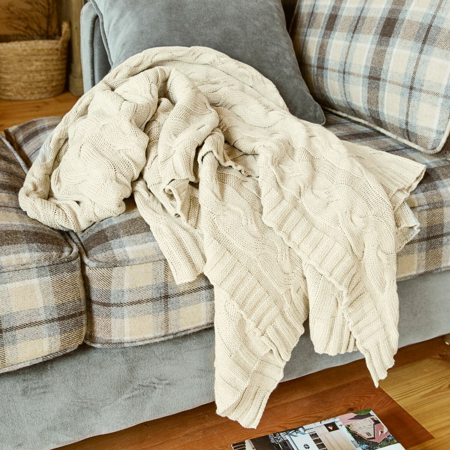 Plaid Arnhem Plaid beige en coton tricoté posé sur un canapé gris à carreaux beige dans un salon