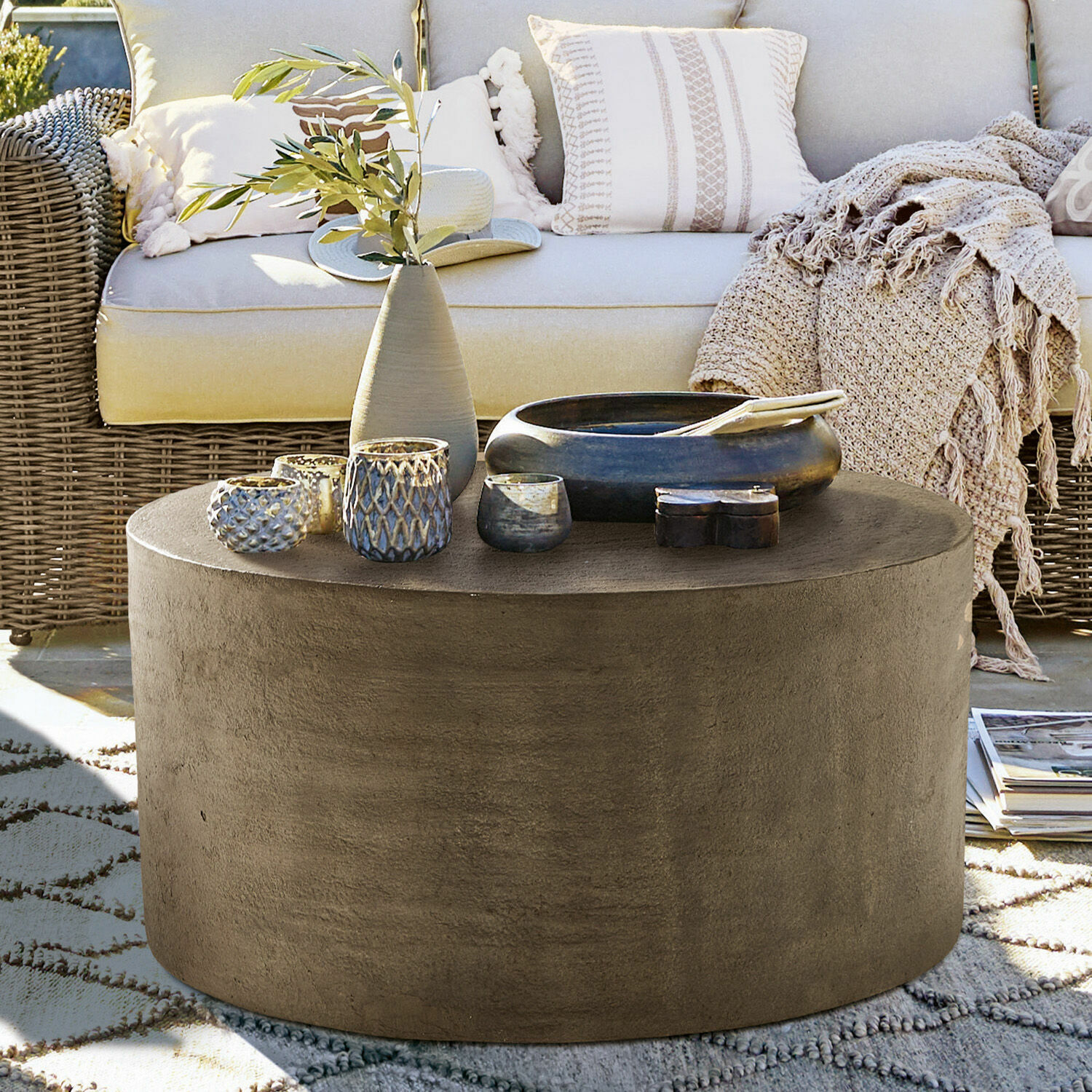 Table basse Lexy Table basse ronde en béton gris avec décorations sur terrasse devant un canapé en rotin beige