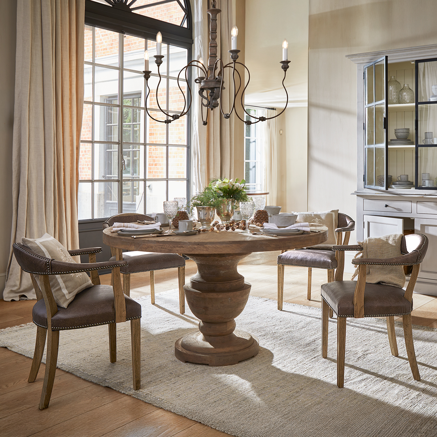 Salle à manger avec table ronde en bois et quatre chaises marron avec coussins, lumière naturelle