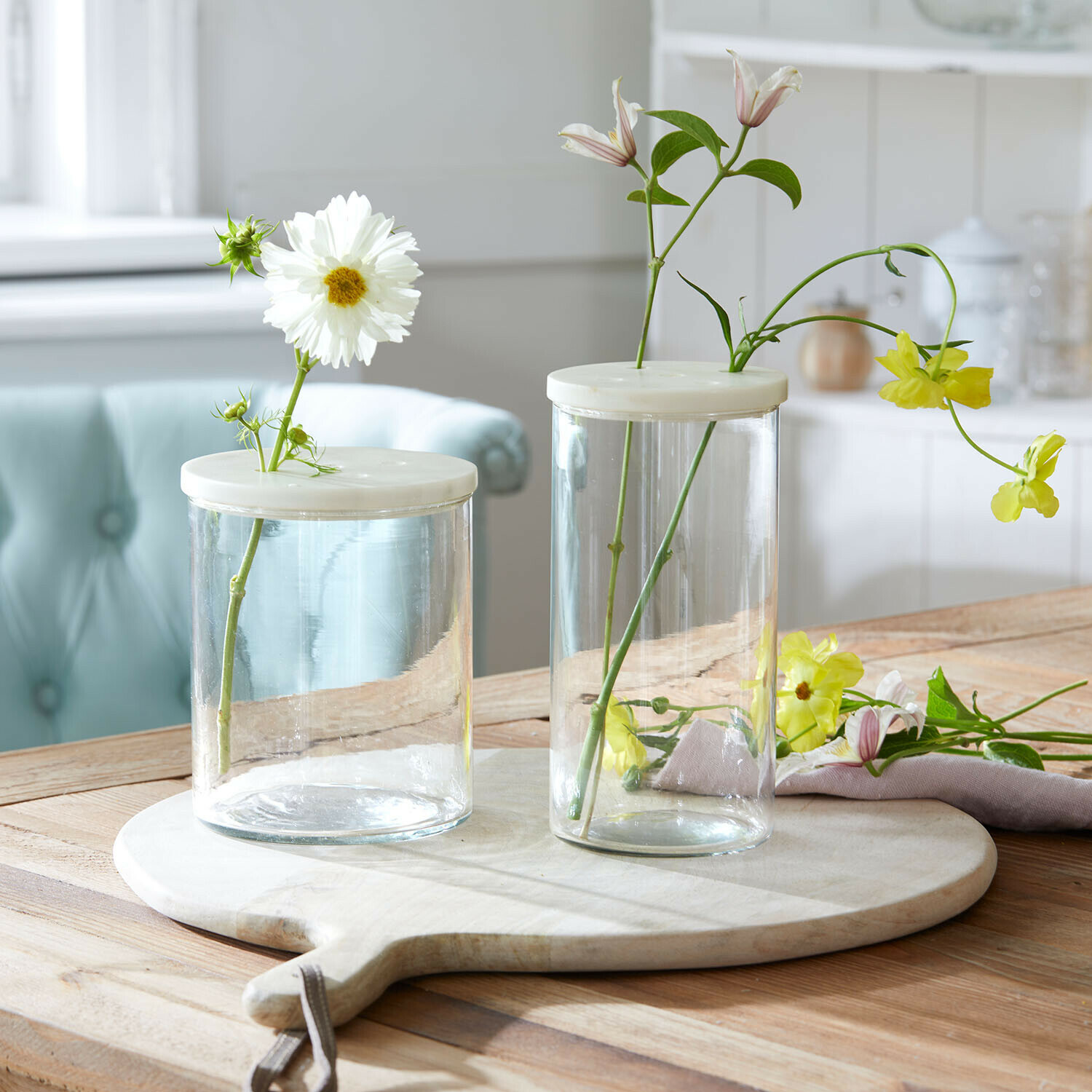 Deux petits vases en verre transparent avec couvercles blancs sur planche en bois avec fleurs délicates