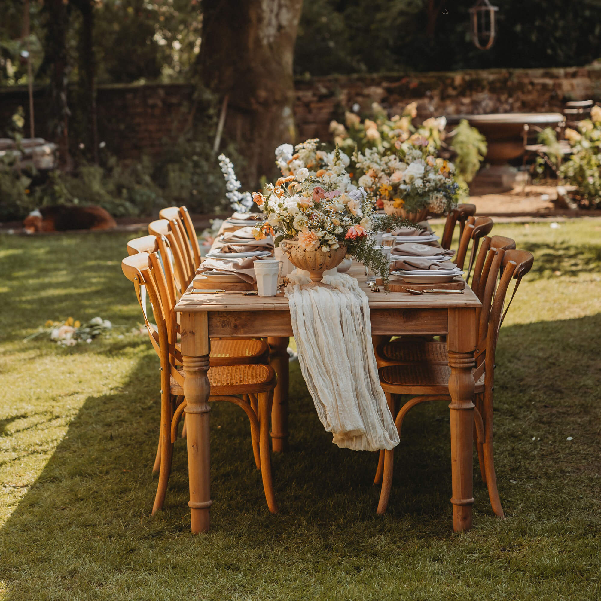 Table de jardin en bois avec chaises et décor floral sur pelouse verte, ambiance extérieure chaleureuse