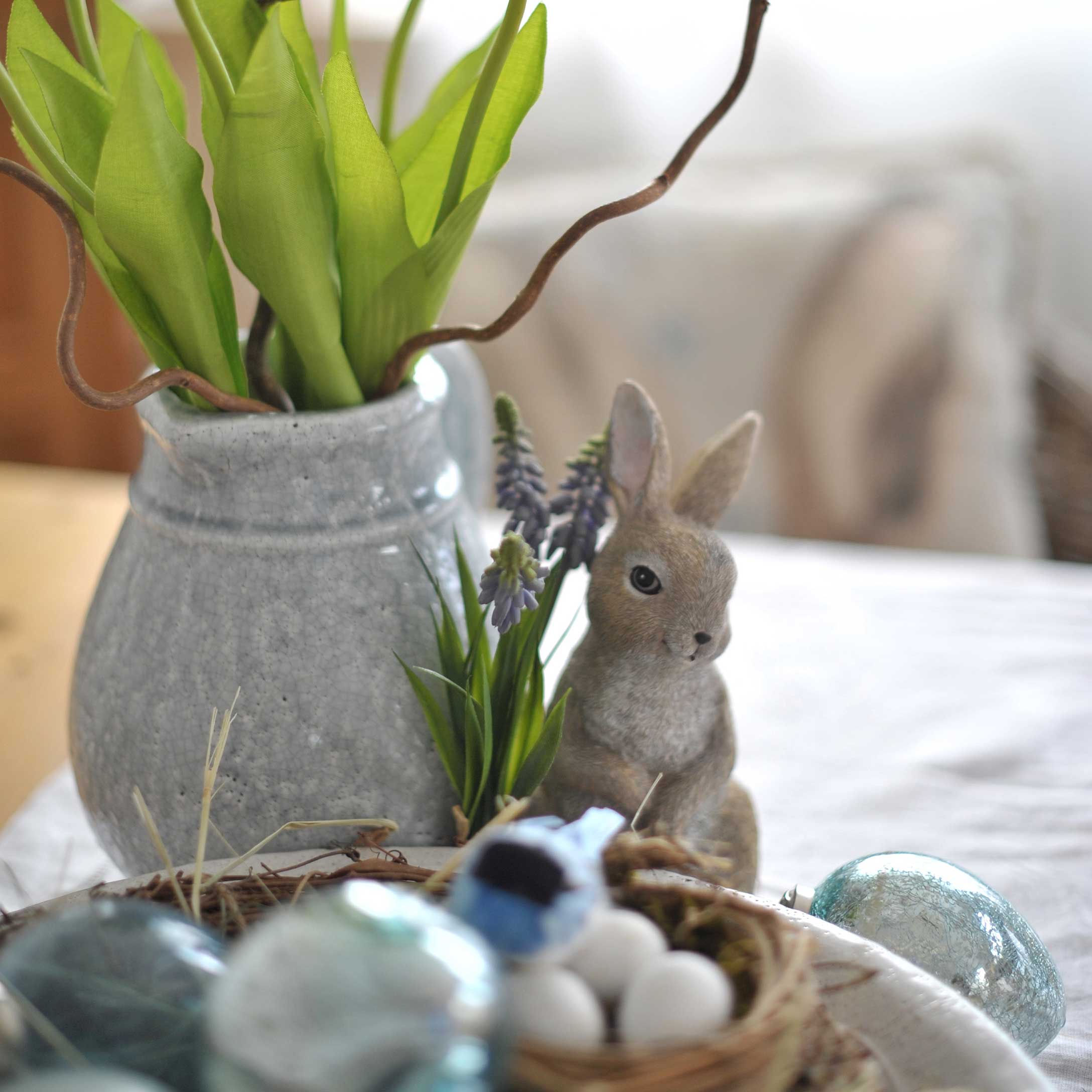 Vase en céramique grise avec feuilles vertes et figurine de lapin sur table décor de Pâques