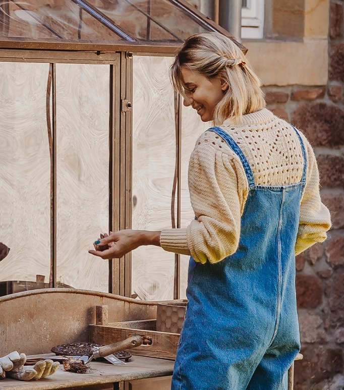 Femme en salopette bleue et pull crème travaillant à une table en bois dans un jardin
