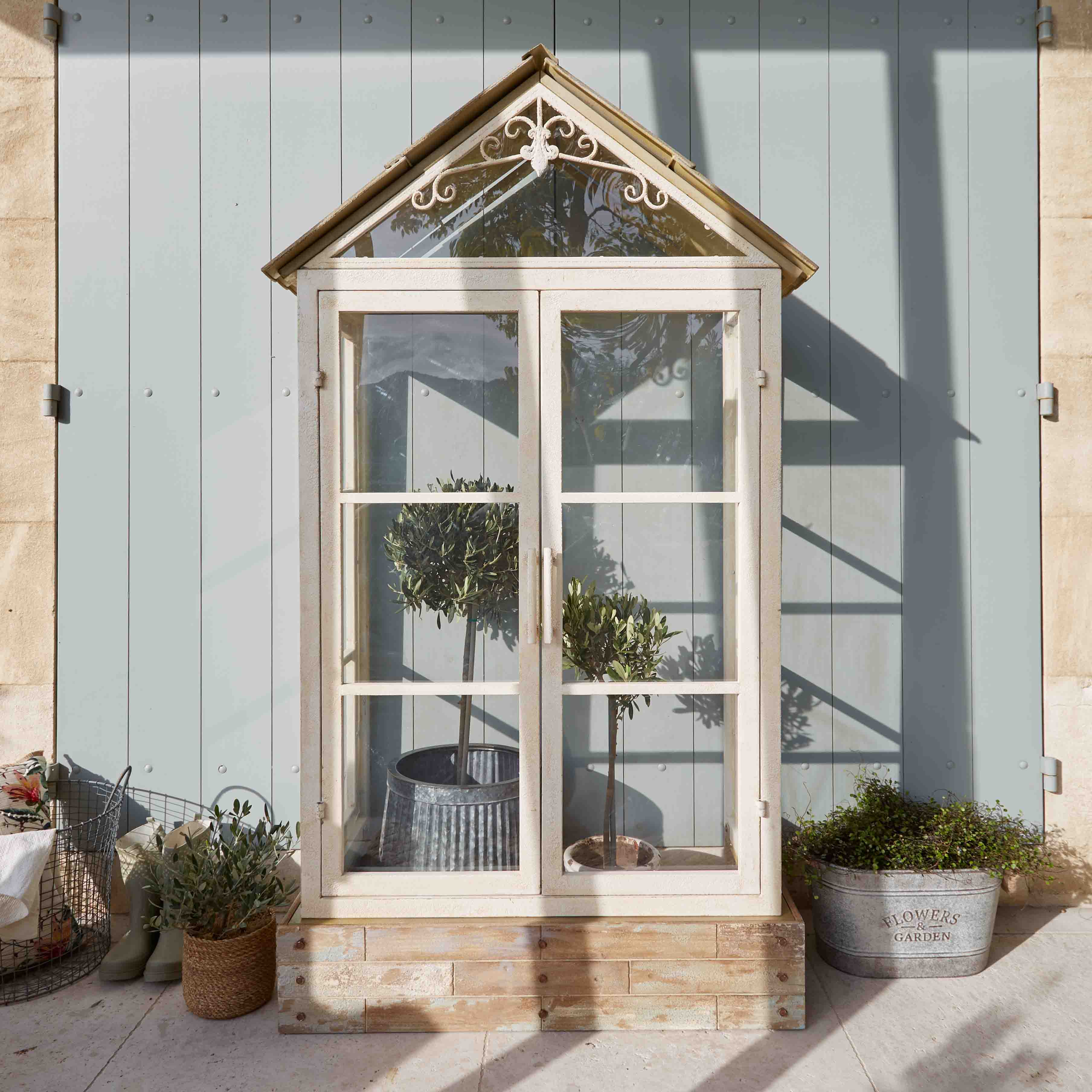 Serre blanche en bois avec toit décoratif et plantes en pots sur une terrasse ensoleillée
