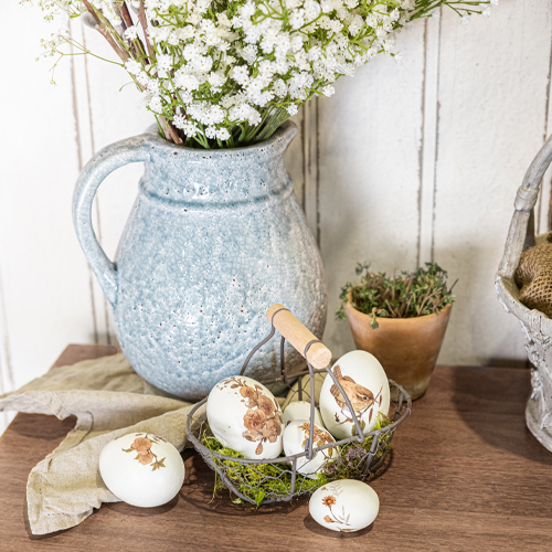 Pichet en céramique bleue avec fleurs blanches et œufs décoratifs à motifs d'animaux sur table en bois