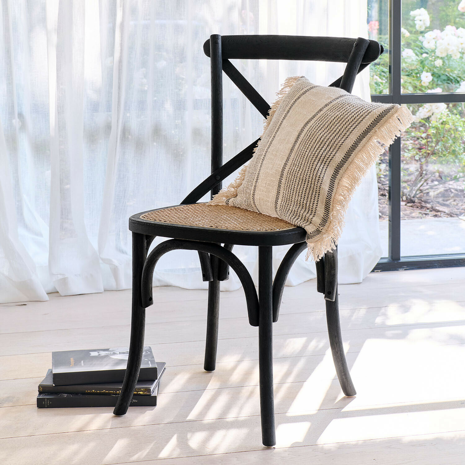 Chaise Kary Chaise en bois noir avec assise en osier et coussin beige à franges dans un intérieur lumineux