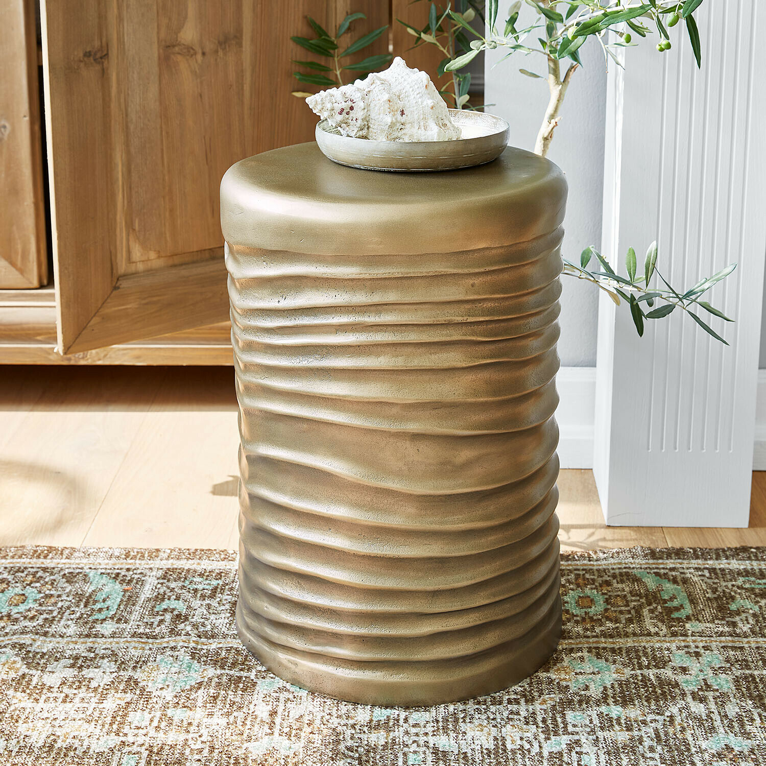 Table d'appoint en métal doré avec texture ondulée posée sur un tapis dans un intérieur lumineux