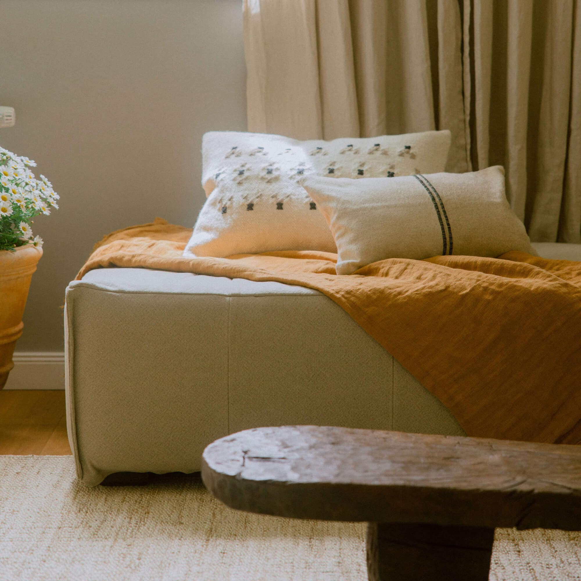 Pouf en tissu beige avec couverture orange et coussins décoratifs dans un intérieur chaleureux