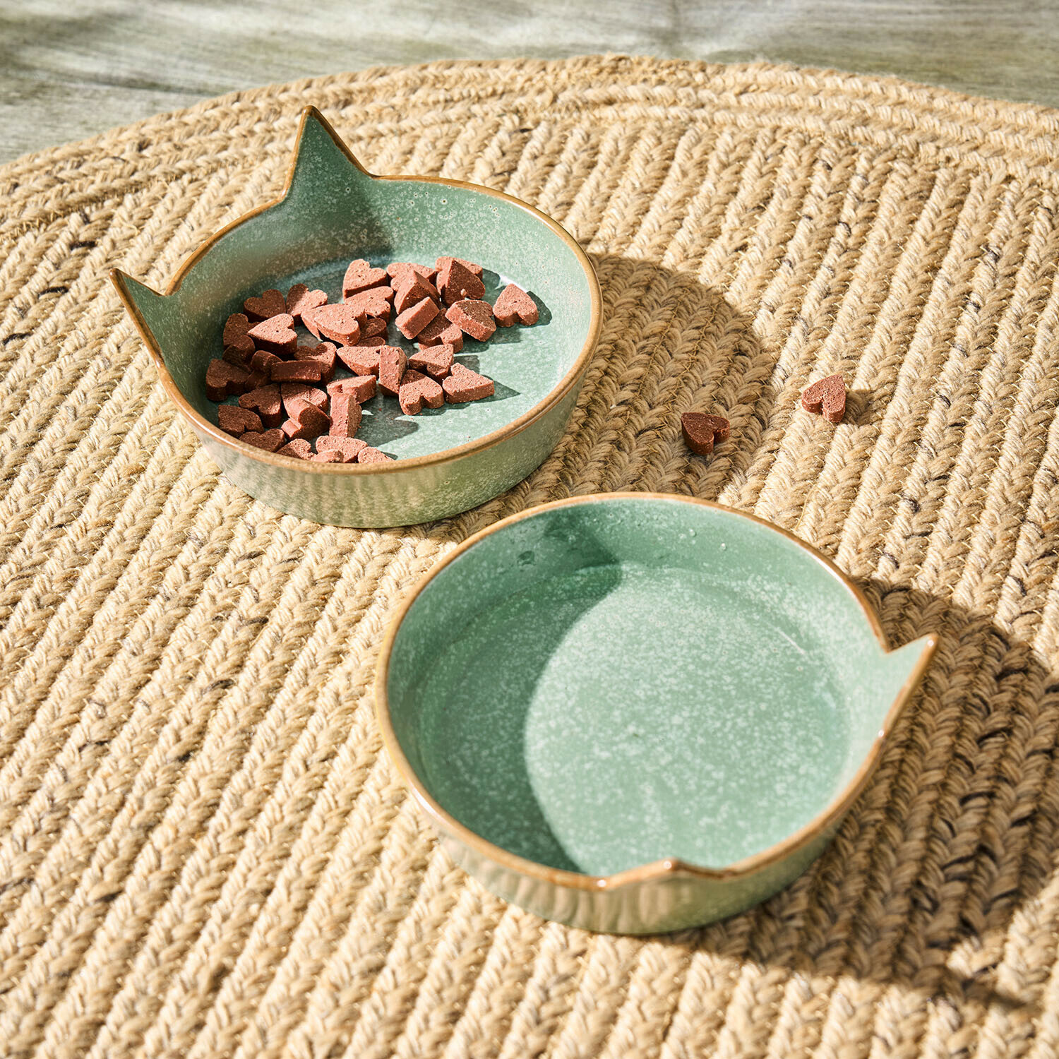 Bol en céramique verte avec oreilles de chat sur tapis tressé, bol avec croquettes en forme de cœur