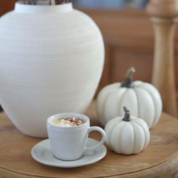 Tasse en céramique blanche avec café et crème fouettée sur table en bois près de citrouilles décoratives blanches et vase