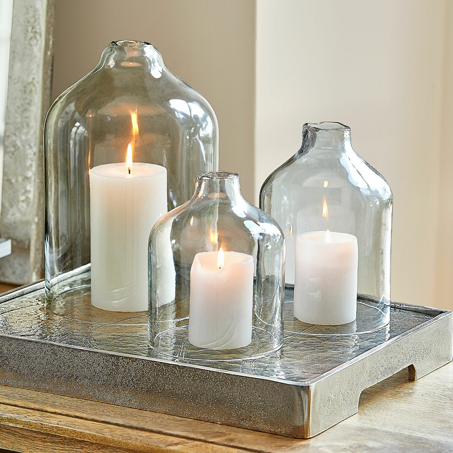 Lot de 4 bougies Braga Trois bougies blanches sous des cloches en verre transparent sur un plateau décoratif en métal