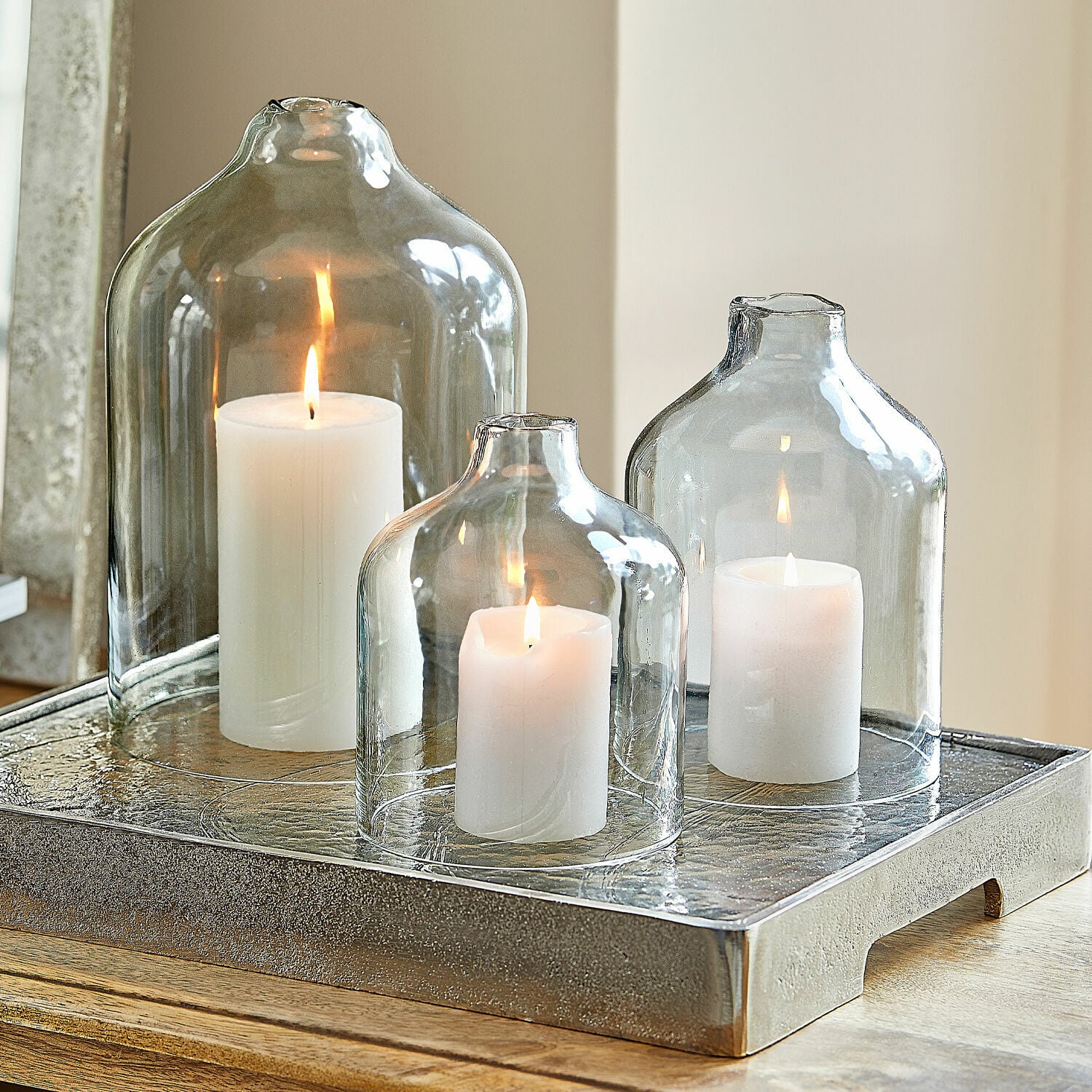 Lot de 4 bougies Braga Trois bougies blanches sous des cloches en verre transparent sur un plateau décoratif en métal