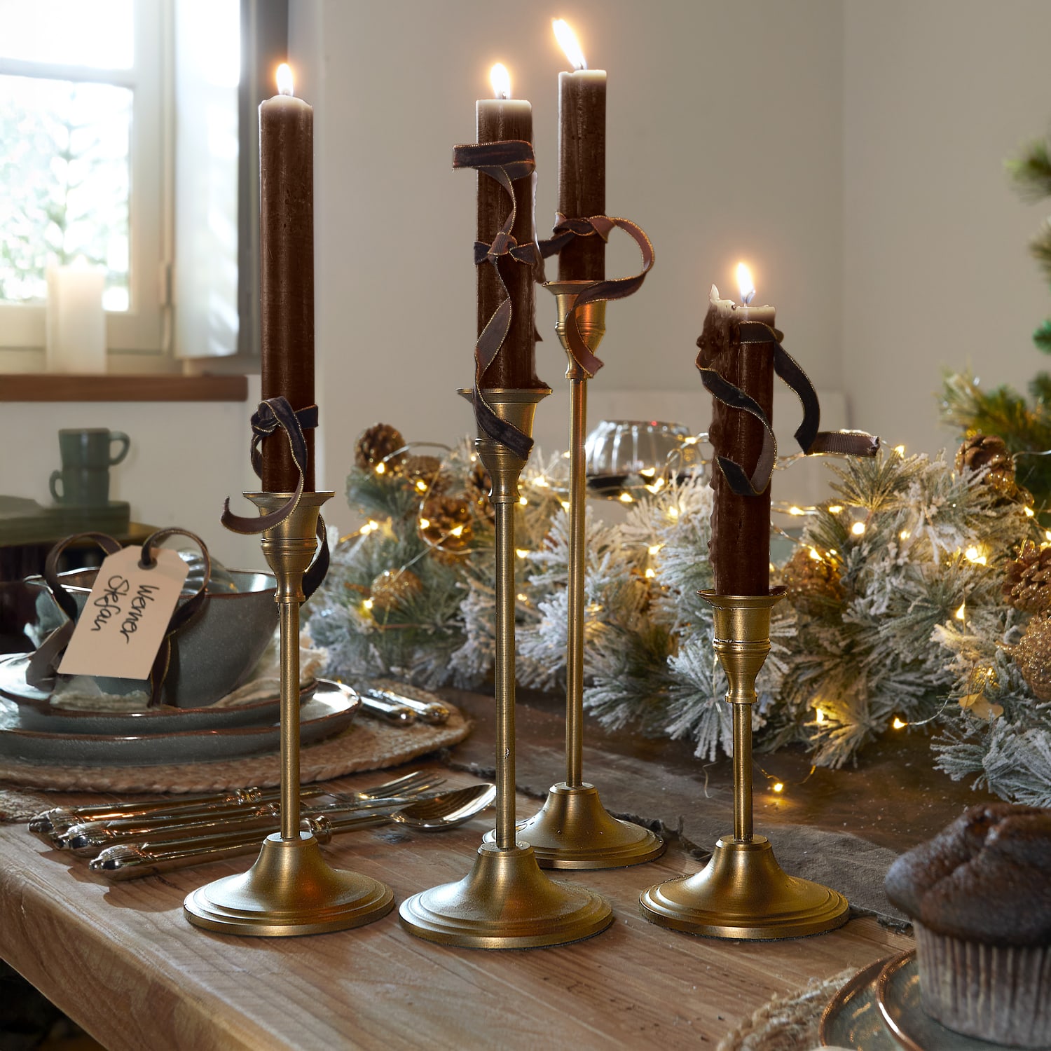 Ensemble de quatre chandeliers dorés avec bougies marron et rubans décoratifs sur une table en bois