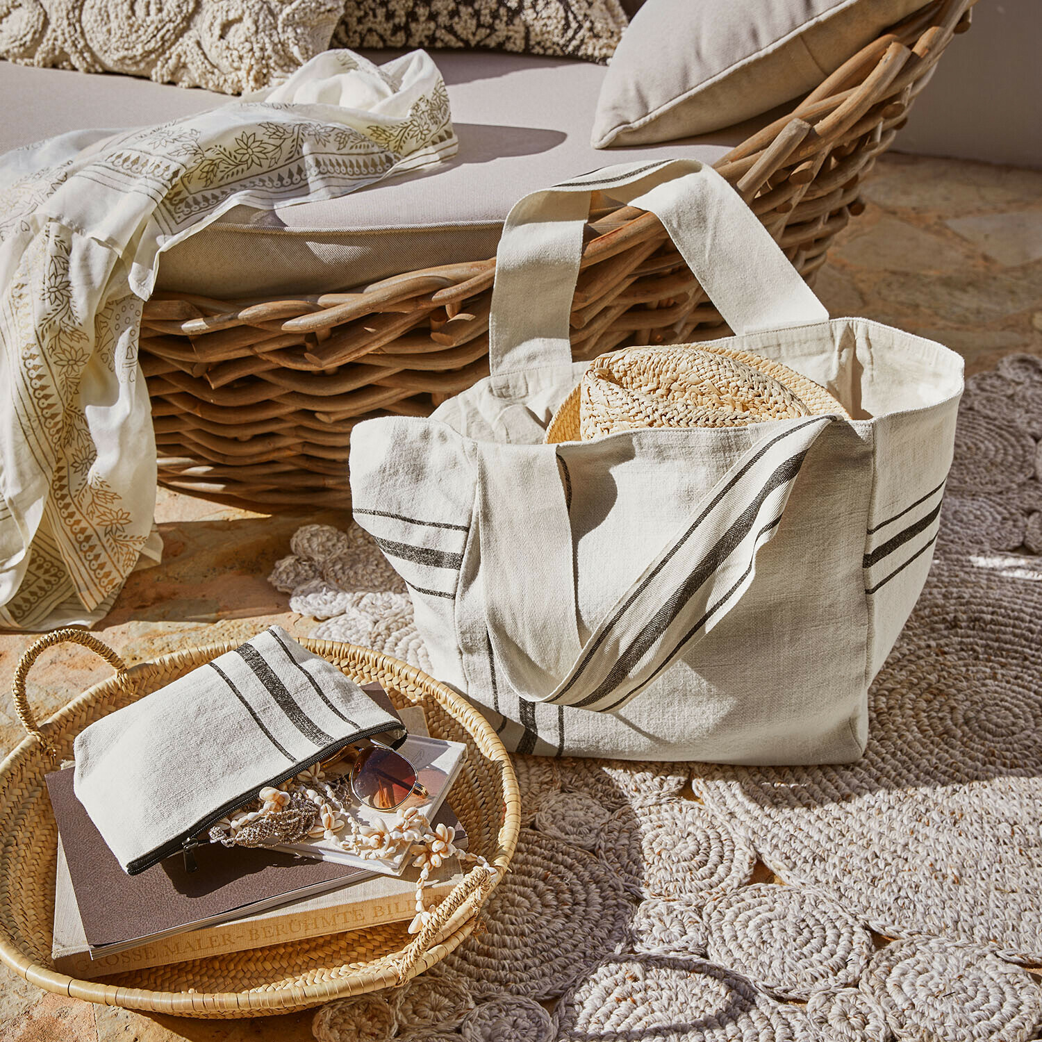 Sac en coton beige avec rayures et chapeau en paille sur fond de fauteuil en osier et tapis