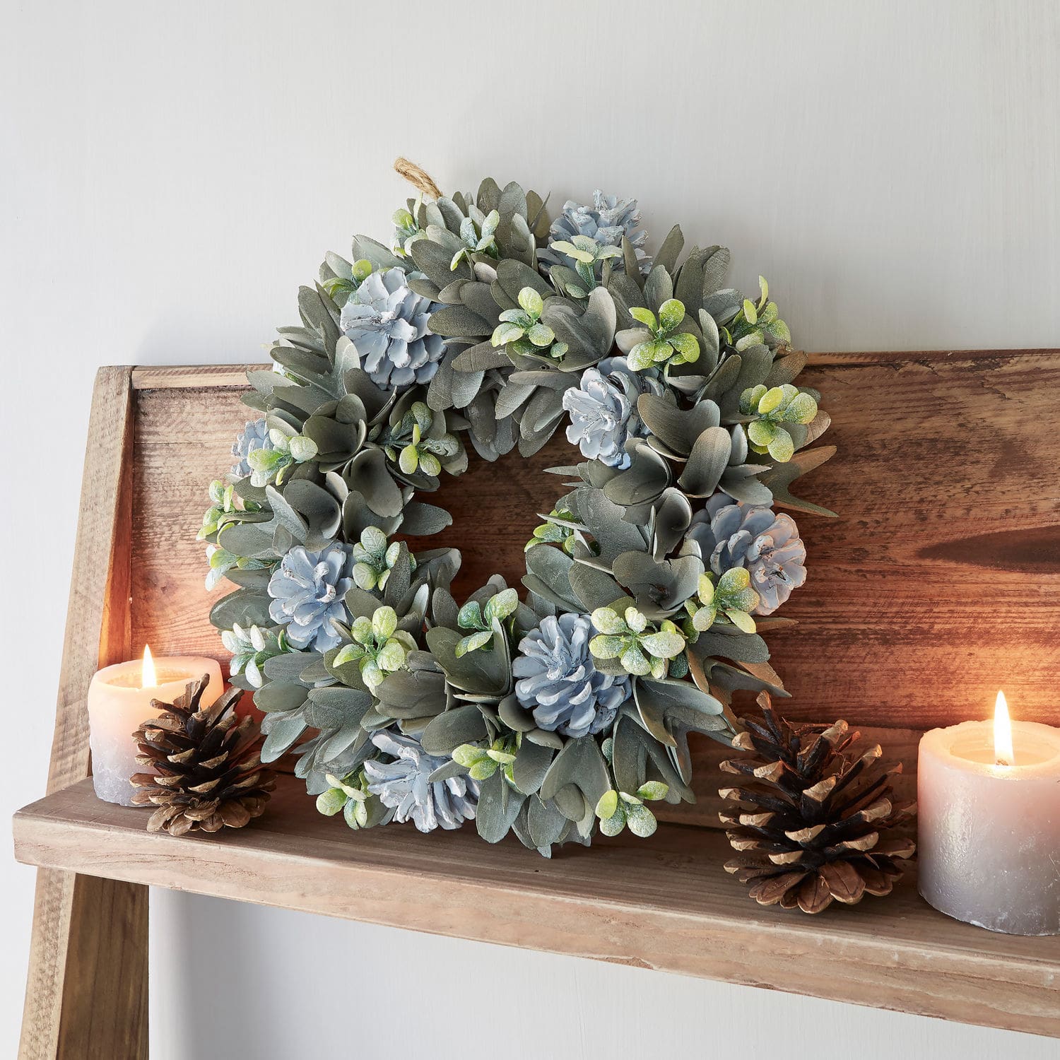 Couronne Deinze Couronne décorative en feuilles grises et pommes de pin bleues sur étagère en bois avec bougies et pommes de pin