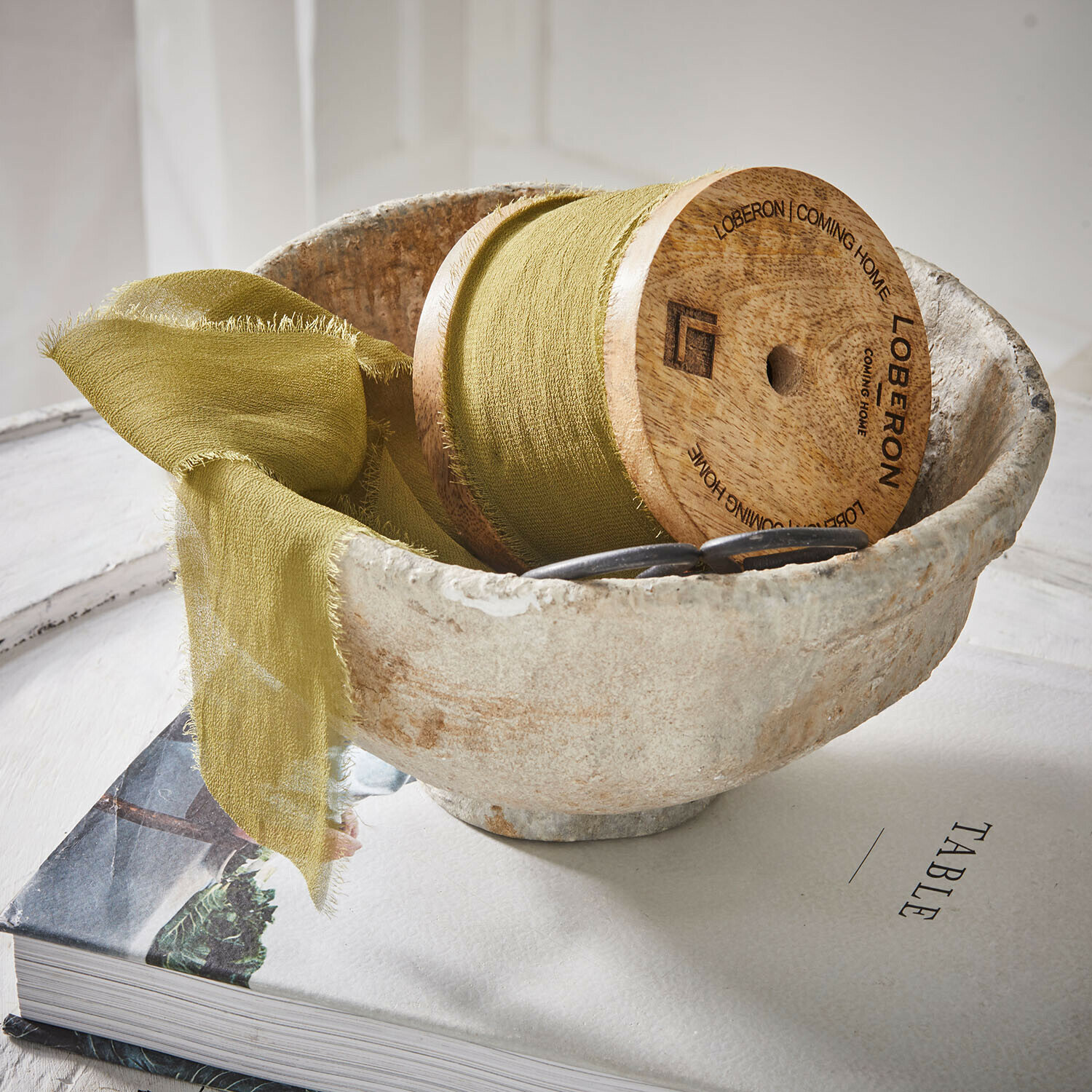 Ruban Lunebrook Bol en pierre naturelle avec tissu vert et bobine en bois posé sur un livre sur la table