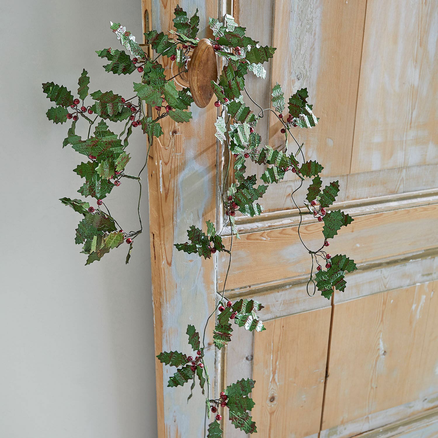 Couronne décorative avec feuilles vertes et baies rouges accrochée à une porte en bois, décoration festive